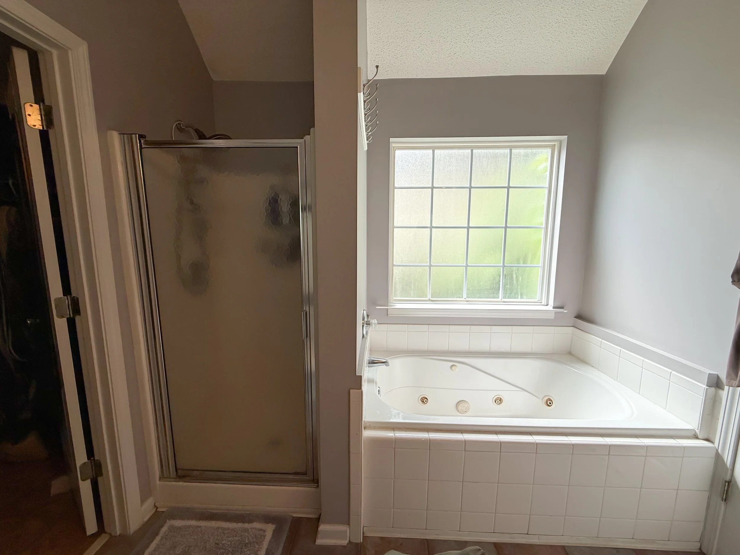 Bathroom with a large window, white tiled shower area, and a gray wall.