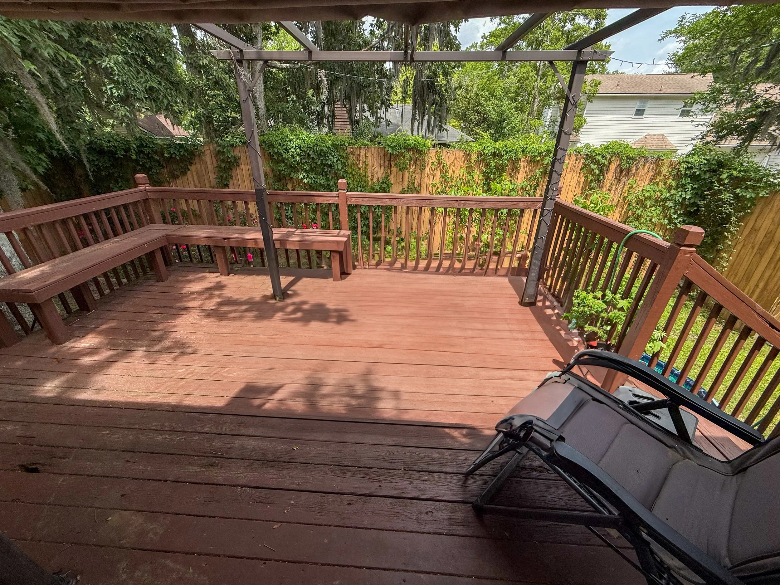 Backyard deck with wooden railing, greenery, and a corner of a pool float or chair in the bottom right corner.