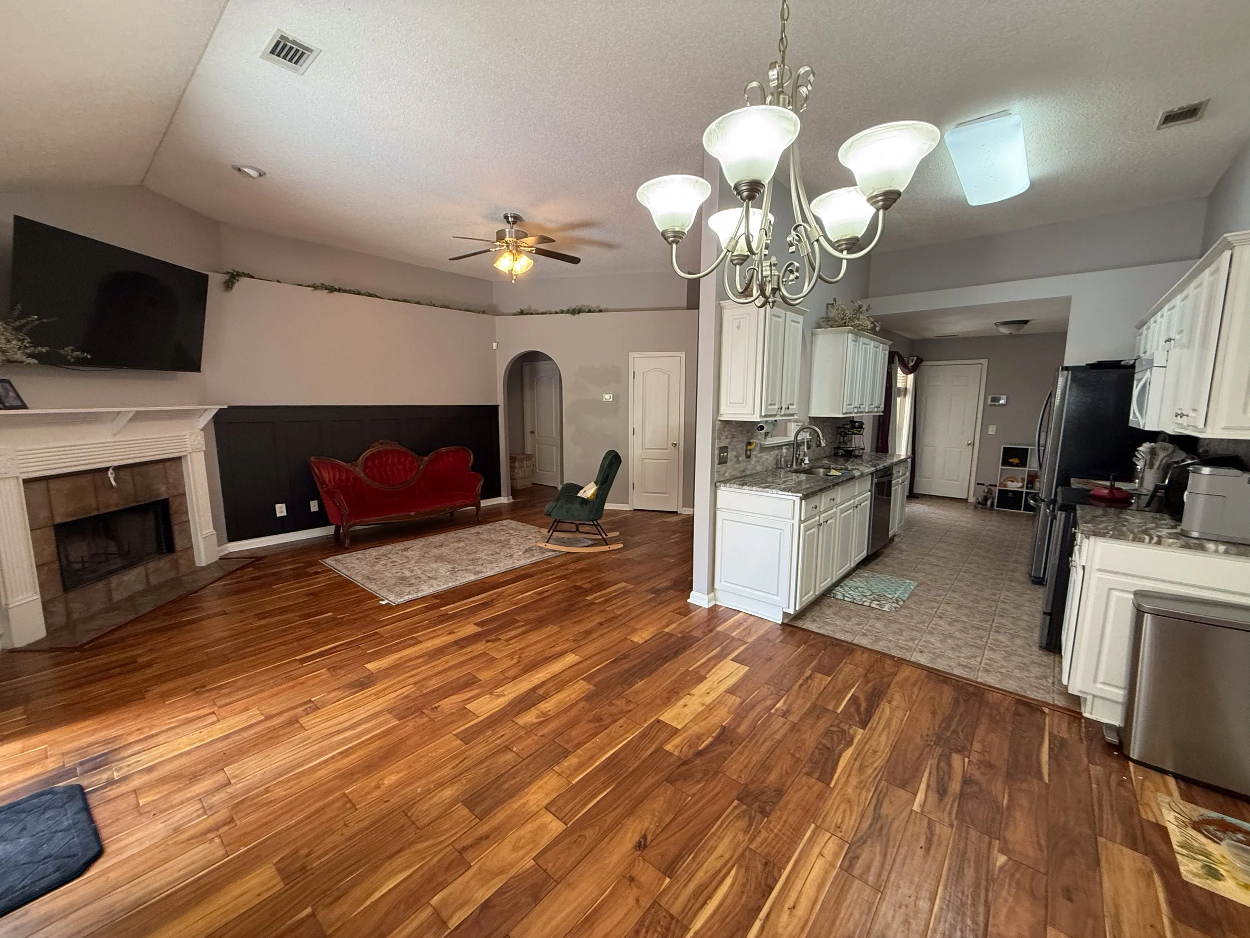 Living room and kitchen area with hardwood floors, a chandelier, a ceiling fan, and white cabinets.