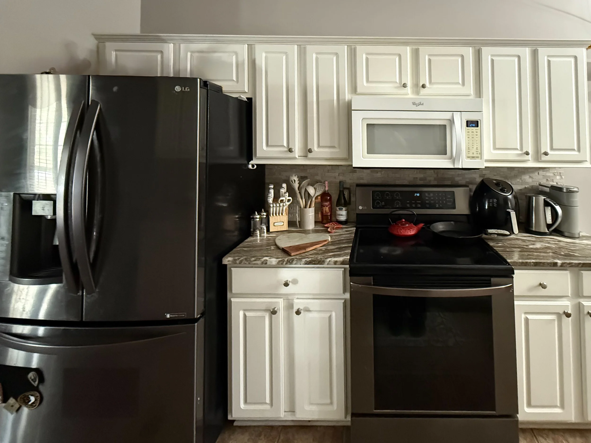 A kitchen with white cabinets, a black refrigerator, a microwave, and a stove, with various kitchen items on the countertop.