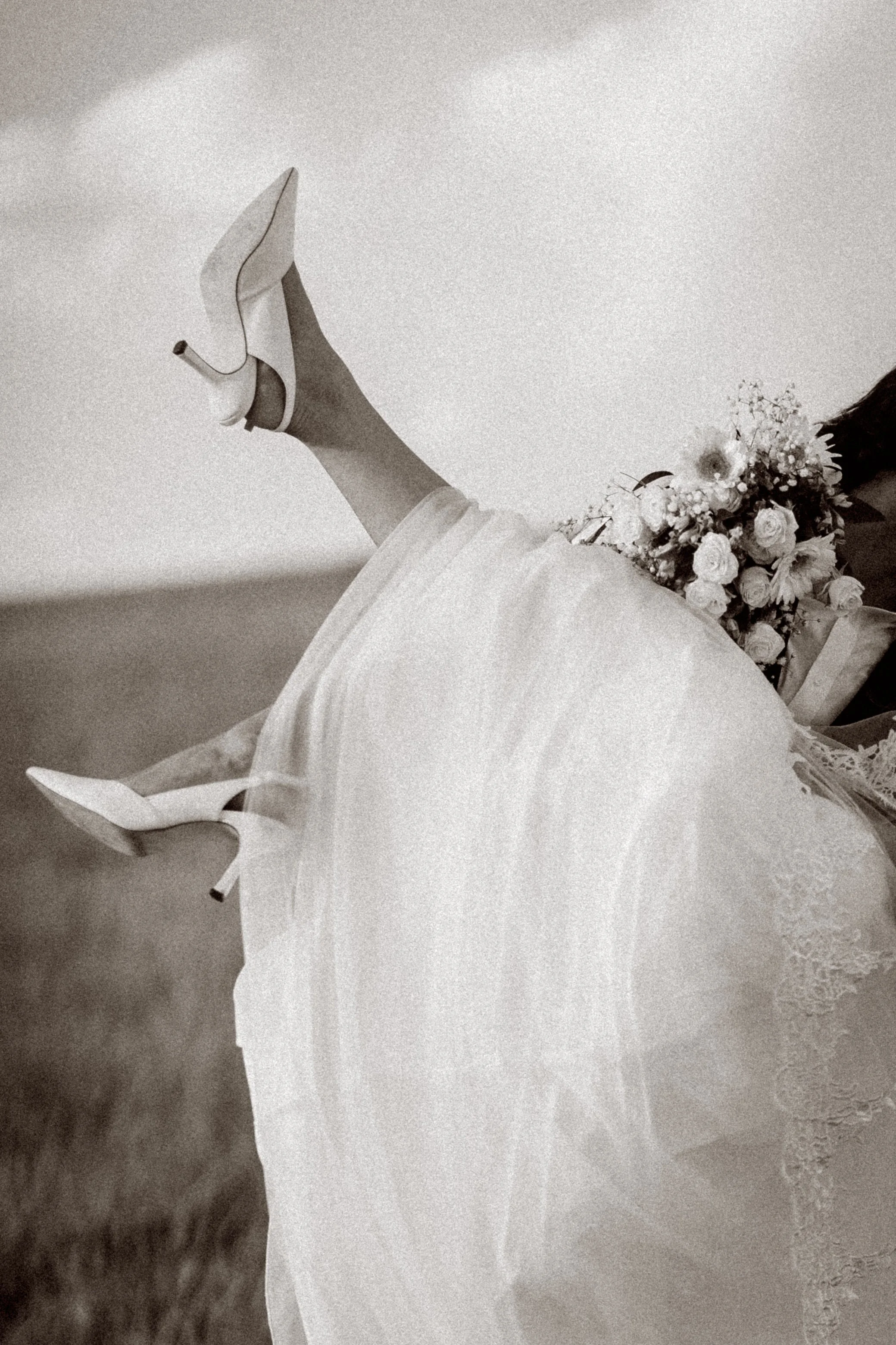 A woman in a wedding dress holding a bouquet of flowers, wearing white high heels, standing on a textured floor.