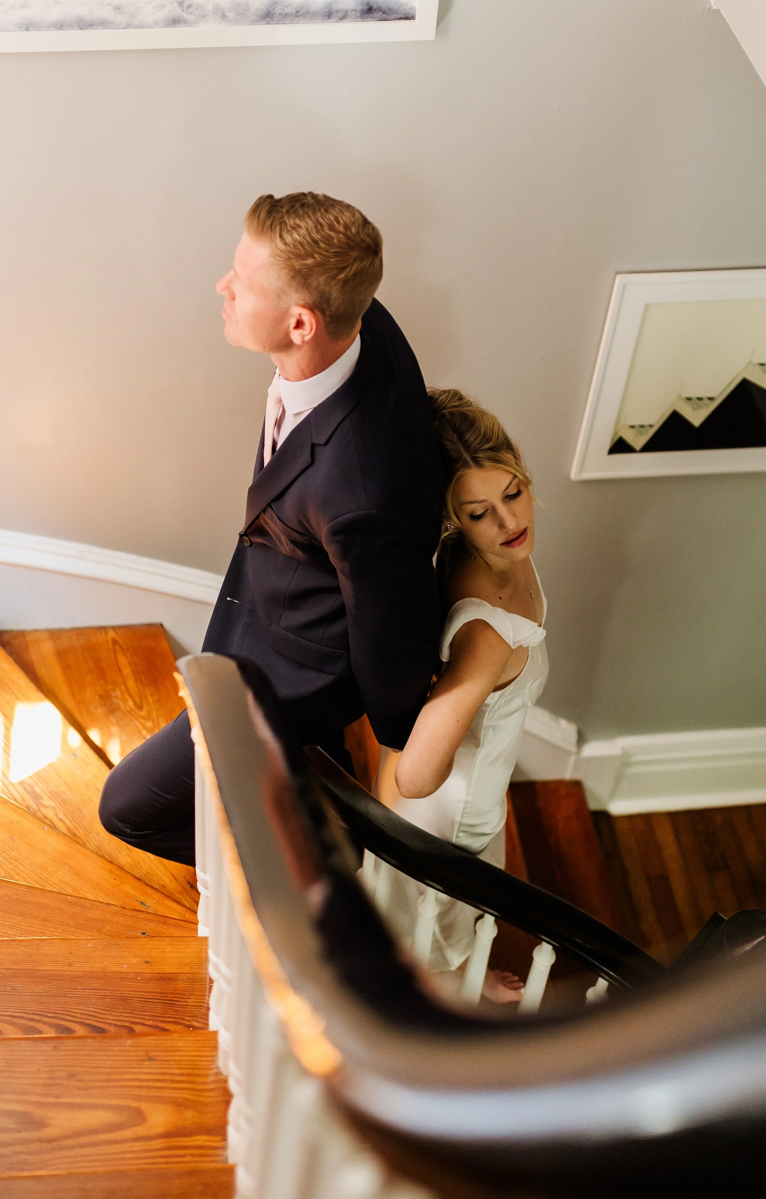 First touch standing back to back on a wooden staircase, looking in opposite directions, framed art in the background.