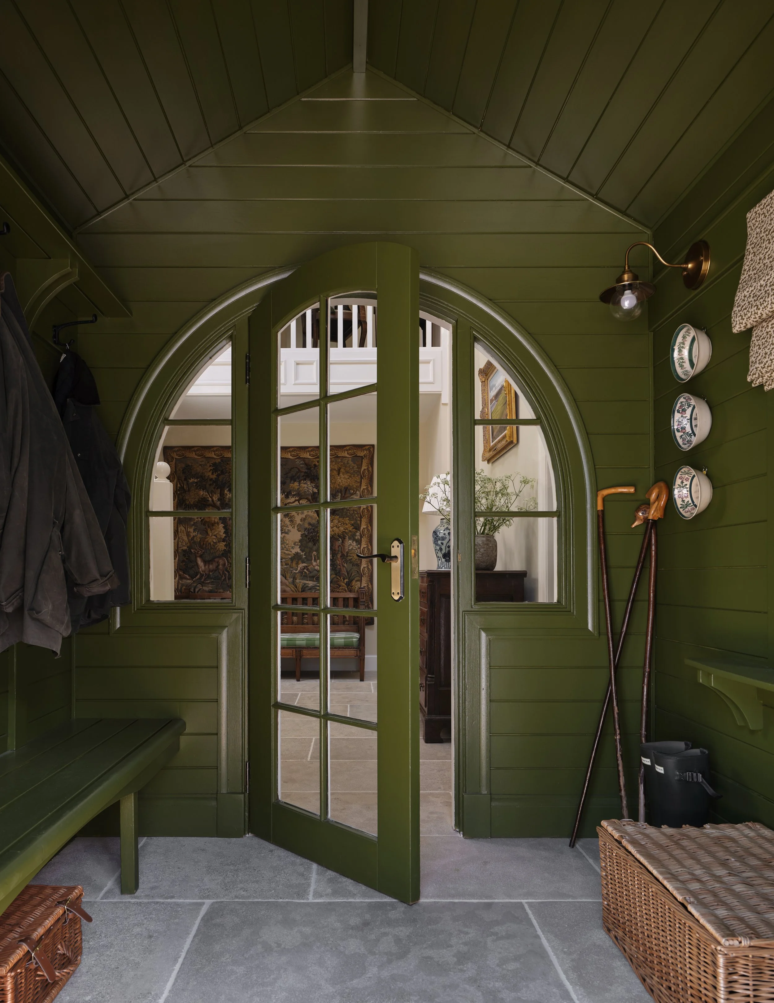 Entryway with green wooden walls and glass door leading to a hallway with a wooden bench, lantern, and paintings.