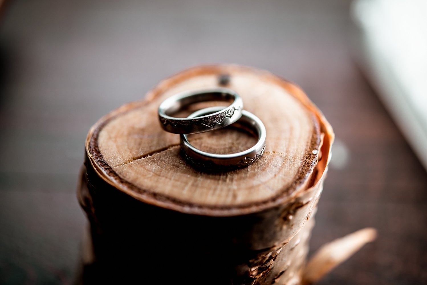 Two silver rings with intricate patterns on a wooden log slice.