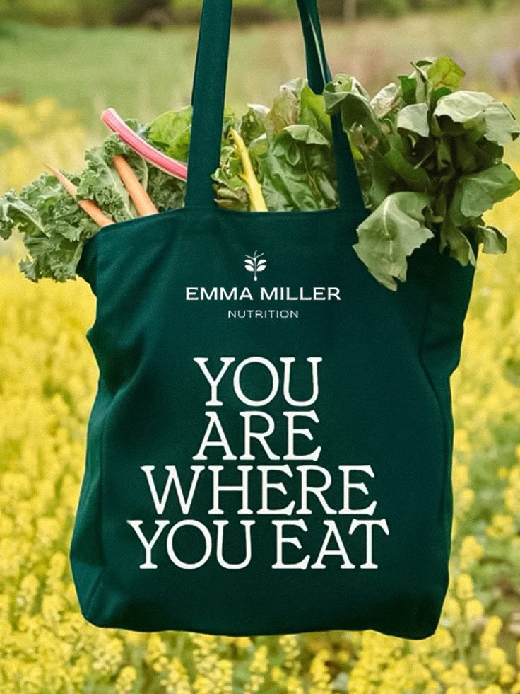 Green reusable tote bag filled with fresh vegetables such as carrots, lettuce, and kale, hanging outdoors.
