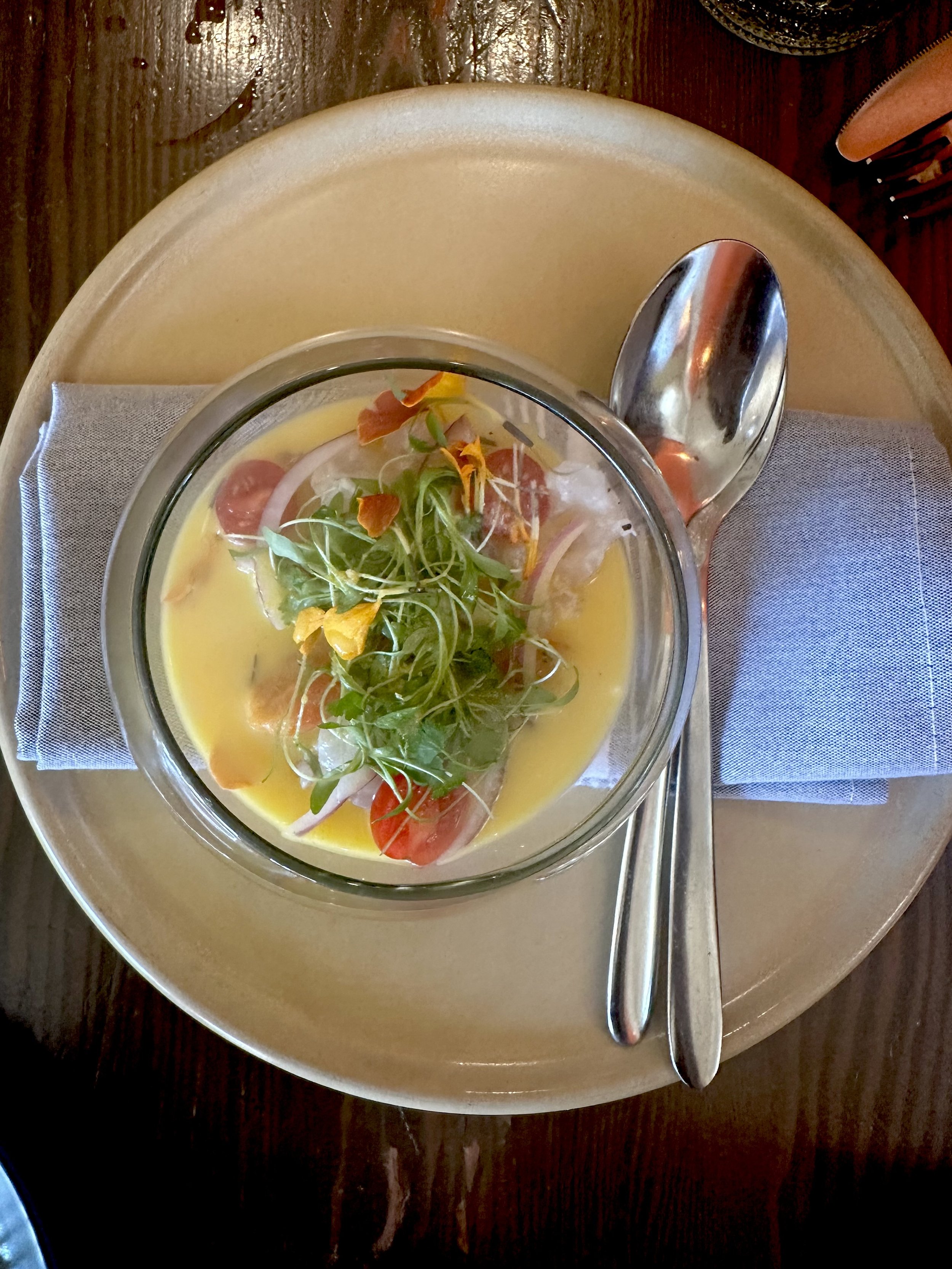 A bowl of salad with lettuce, cherry tomatoes, onion slices, and edible flowers on a plate, with a silver spoon resting on a folded gray napkin.