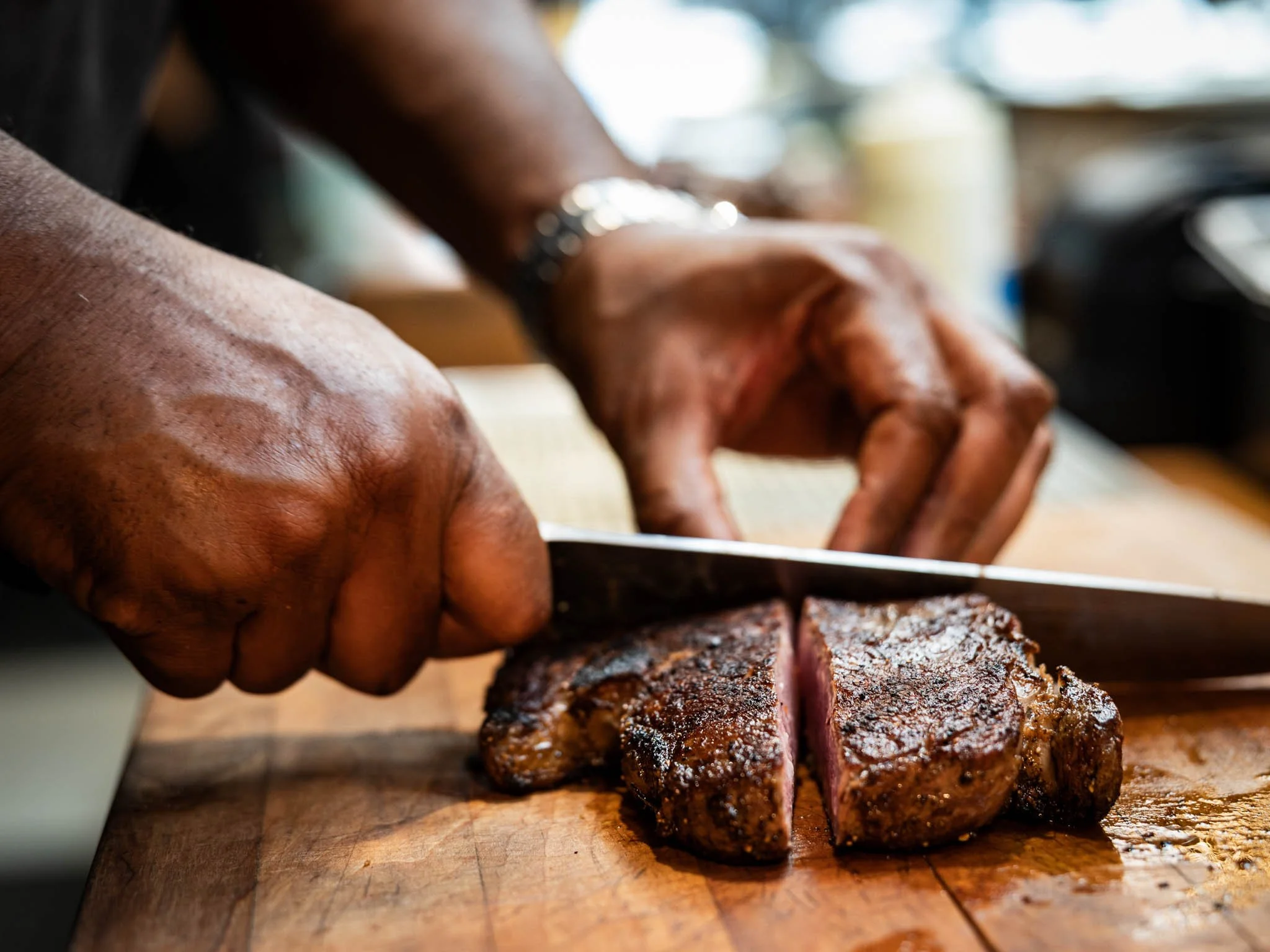 A person slices a cooked steak on a wooden cutting board.