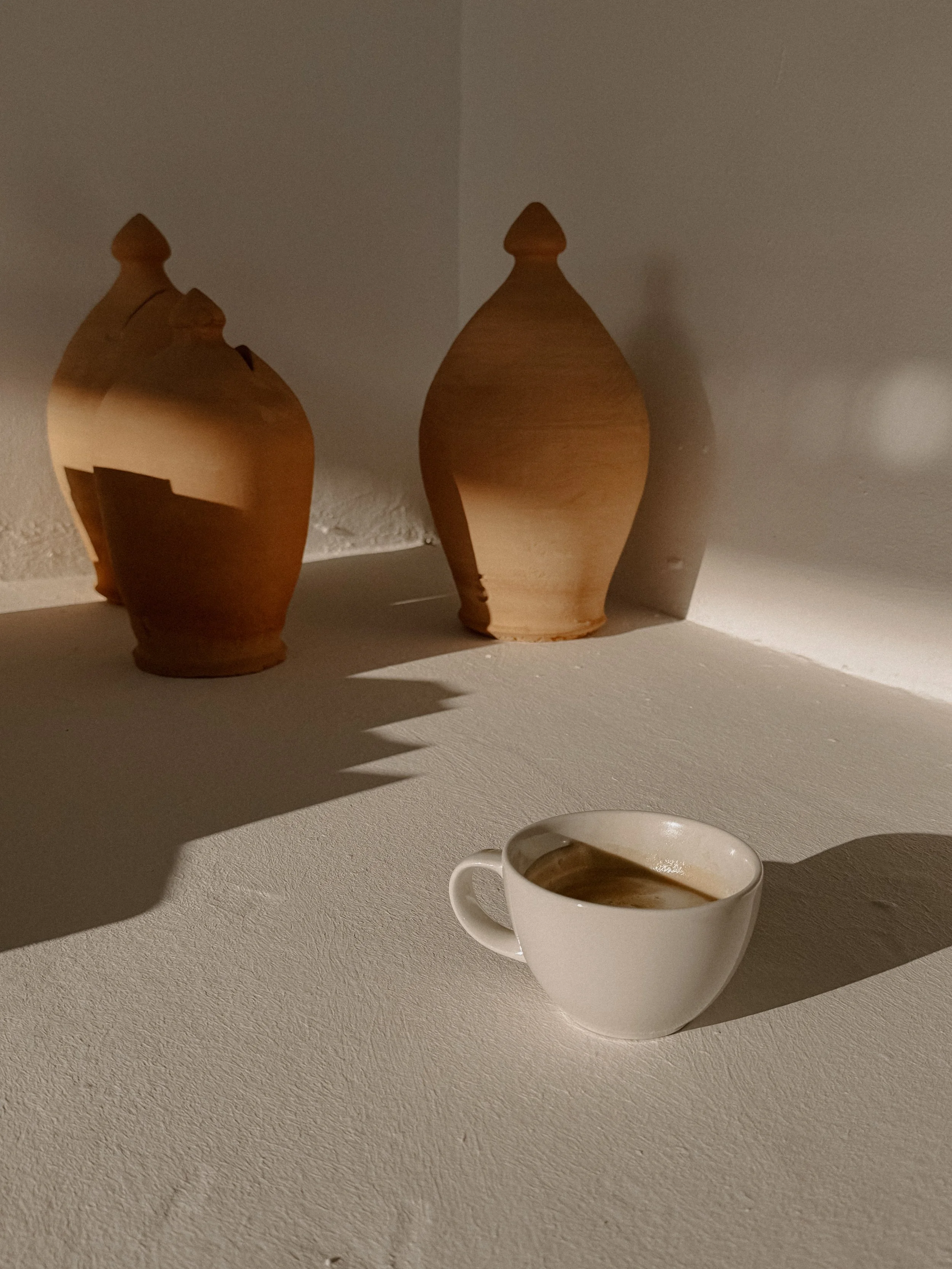 Stilleben: Zwei tonartige Vasen auf einer weißen Oberfläche, eine weiße Kaffeetasse, Schatten auf der Oberfläche.