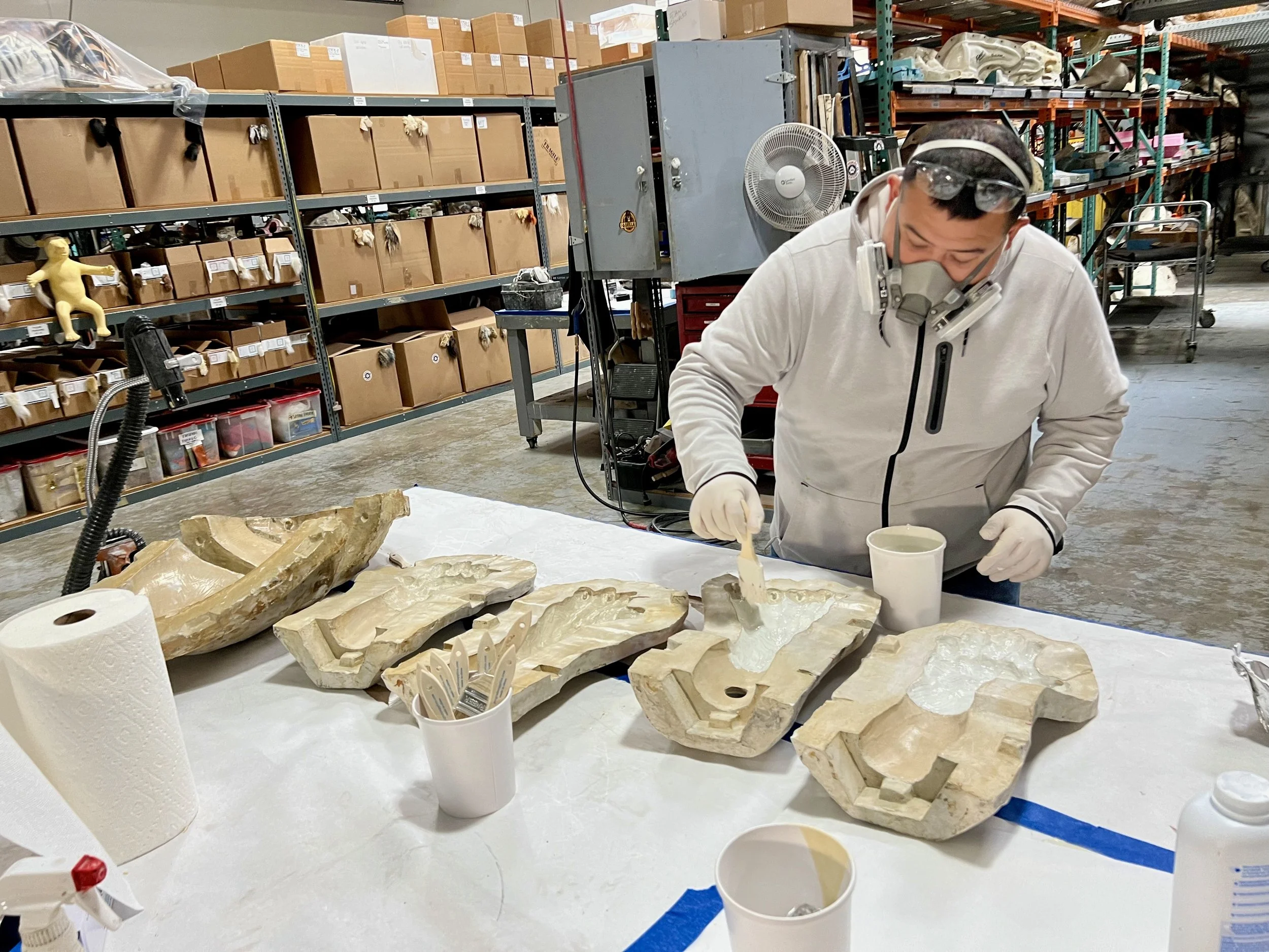 Artist lays coats of latex material into bear paw molds to create bear paw gloves.