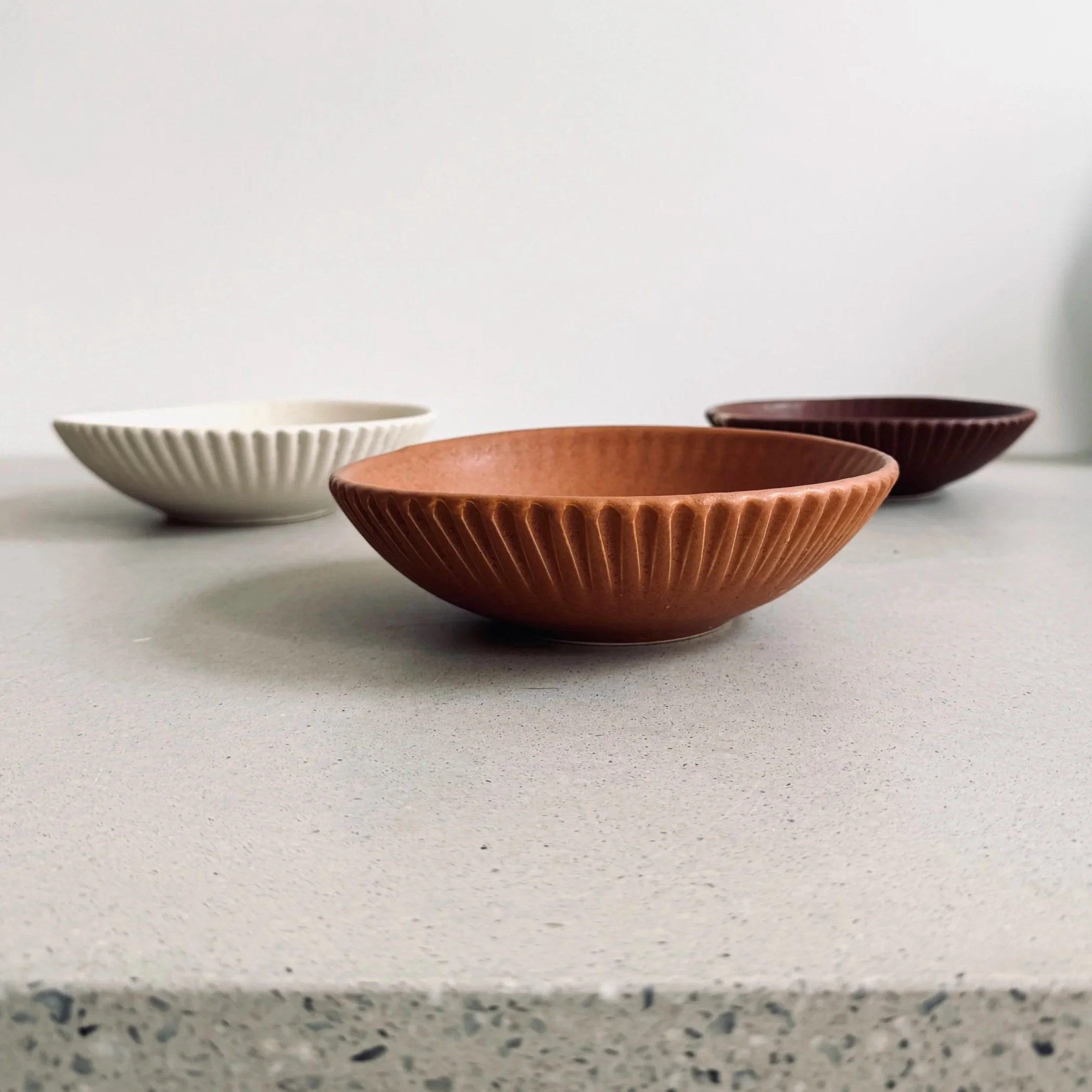 Slip-cast fluted porcelain Moon Bowl in Canyon, Moonlight, and Rosewood glazes on terrazzo surface — Myrth Ceramics