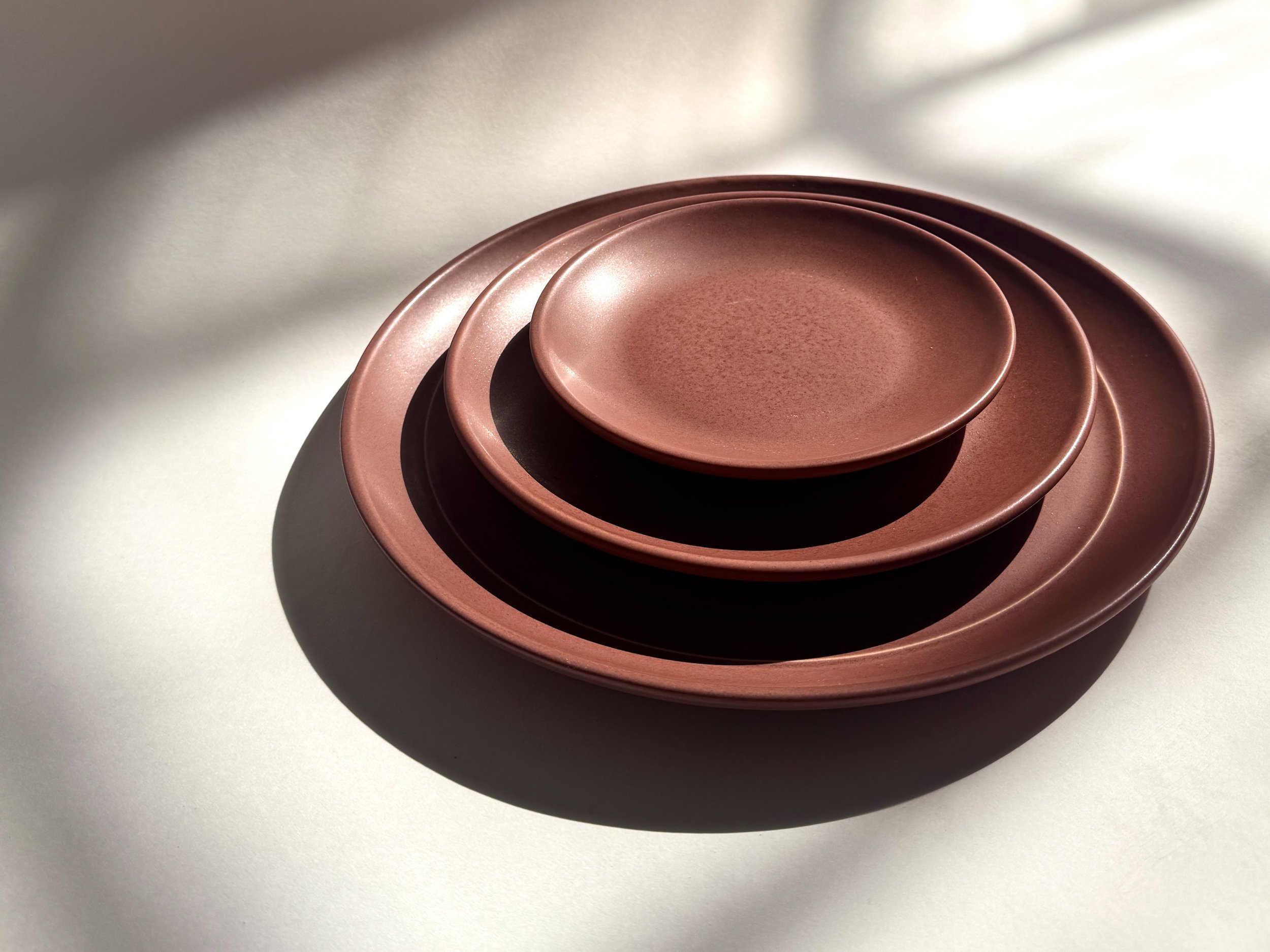 A Brandywine porcelain plate, dusty red with fine speckle across a satin matte surface.