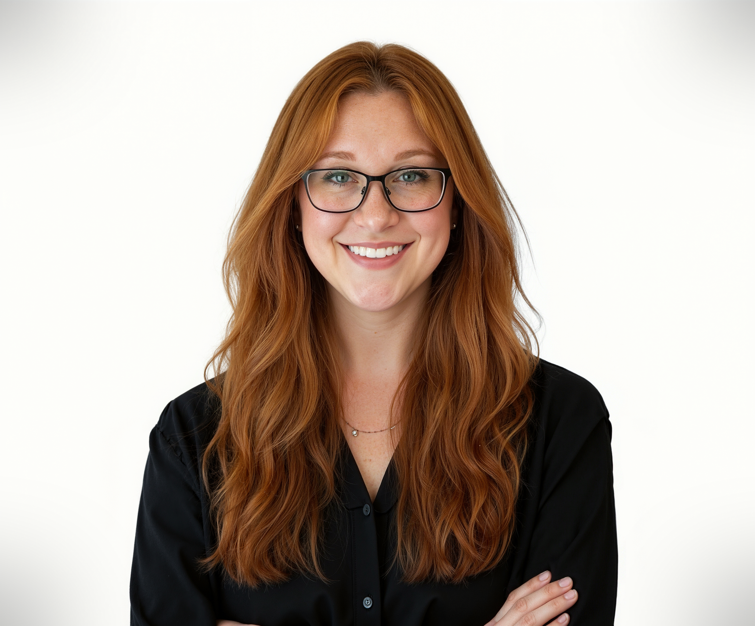 A woman with red hair, wearing glasses and a black shirt, smiling with her arms crossed against a plain white background.