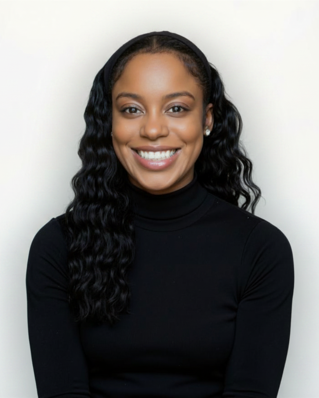 A young woman with curly black hair, wearing a black turtleneck, smiling, against a plain white background.