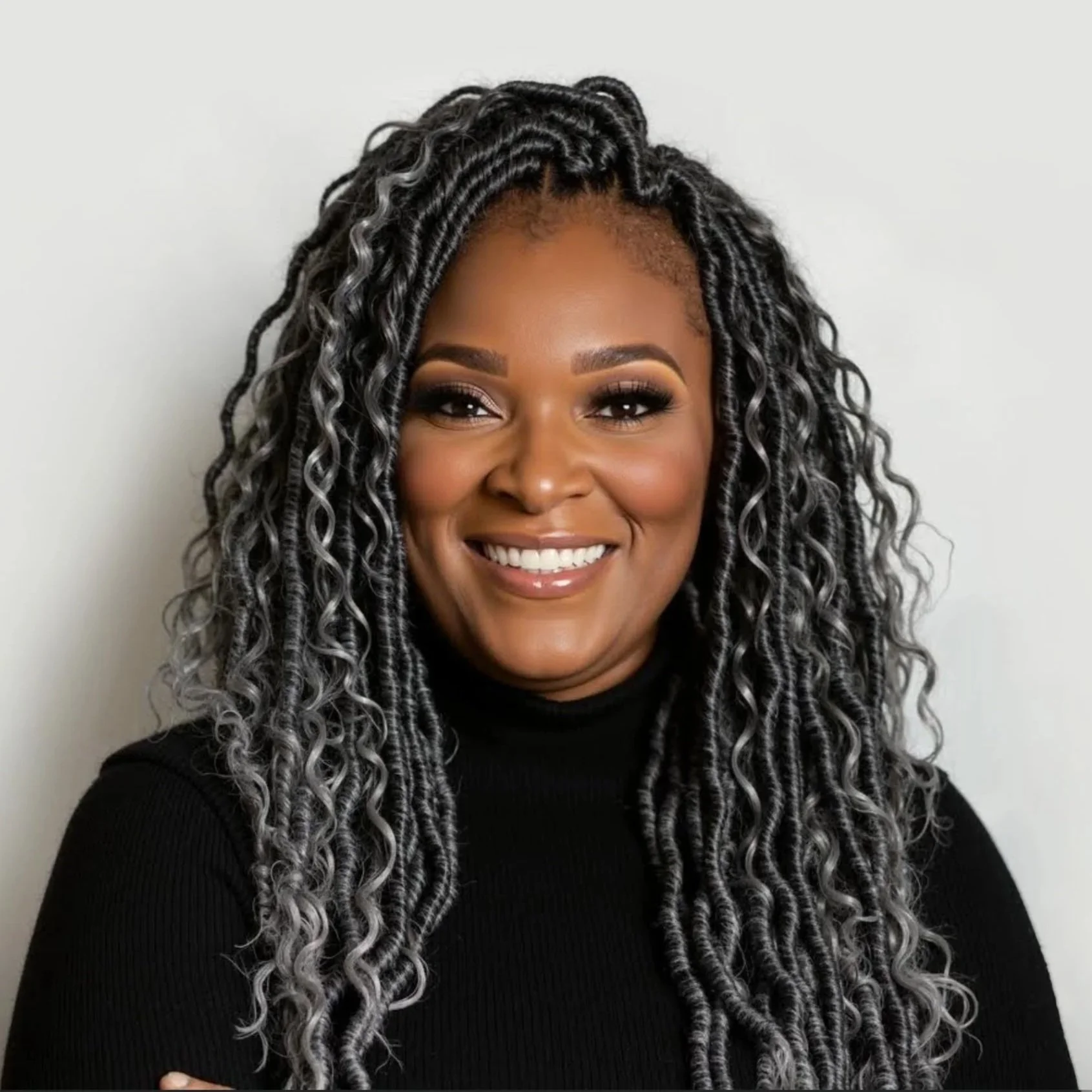 Portrait of Cerita Yvonne with long curly hair, wearing a black turtleneck, smiling softly against a plain gray background.