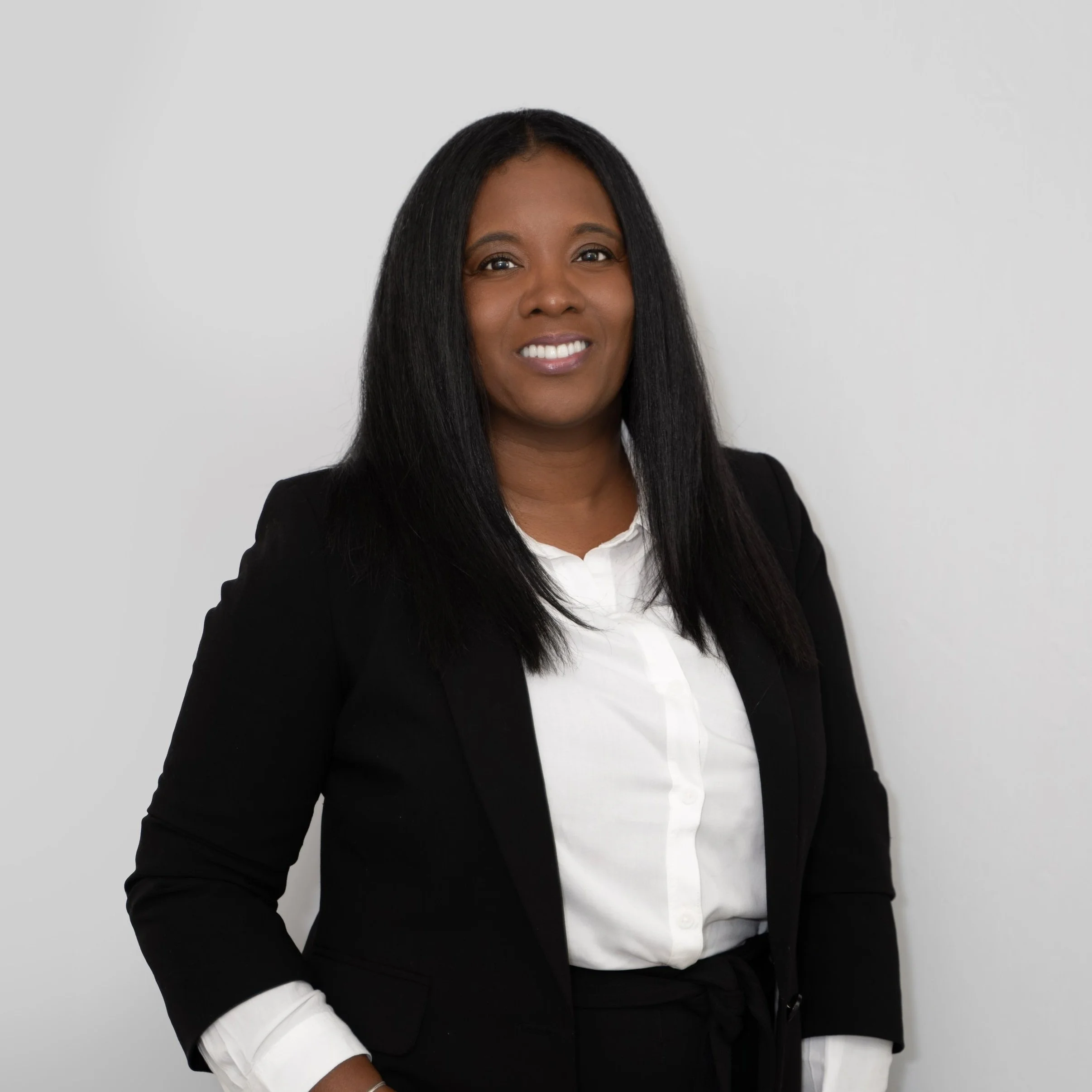 Santwaa Covington smiling, wearing a black blazer and white shirt, standing against a plain white background.