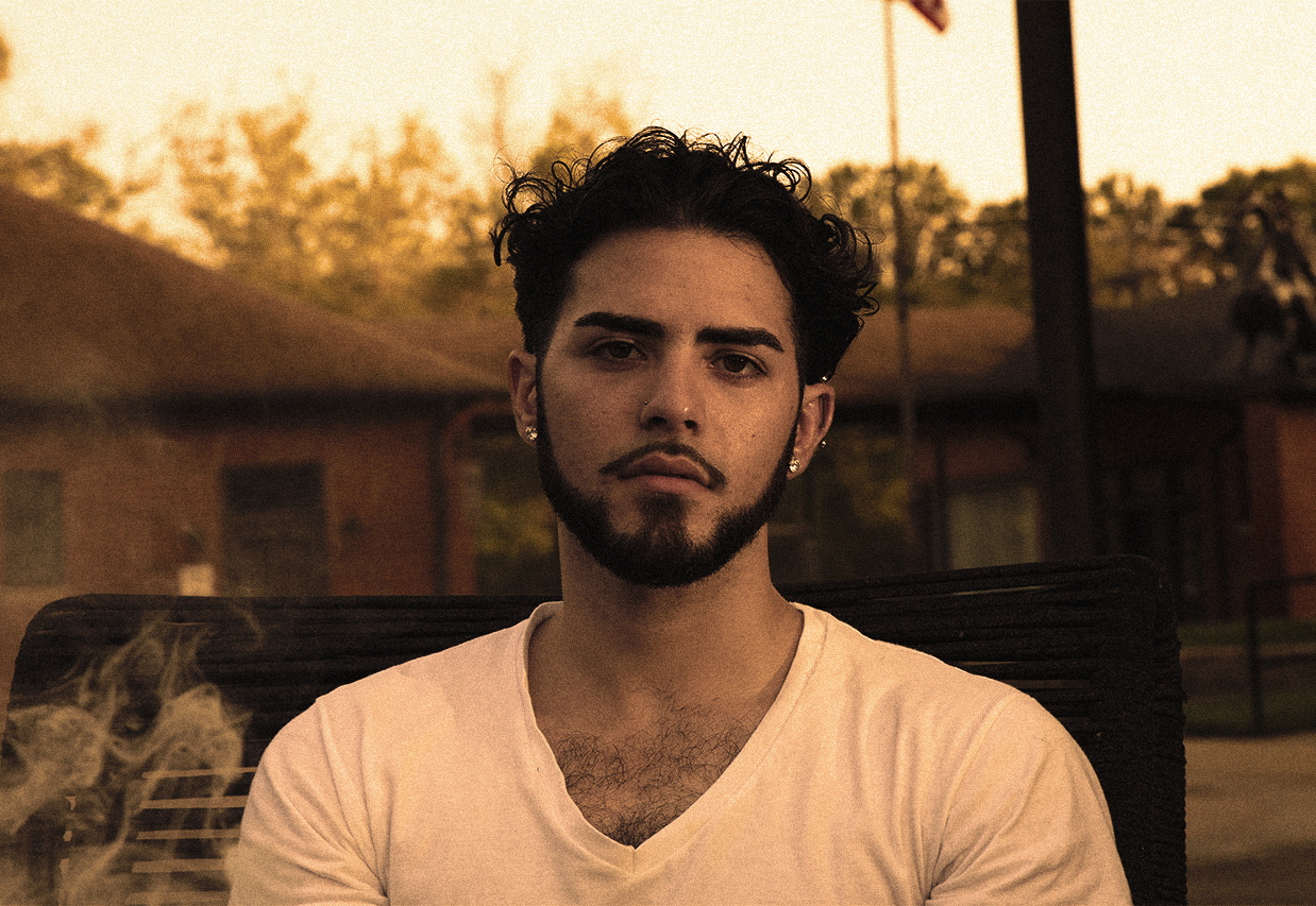 Young man staring at camera while sitting on a bench in front of a flagpole