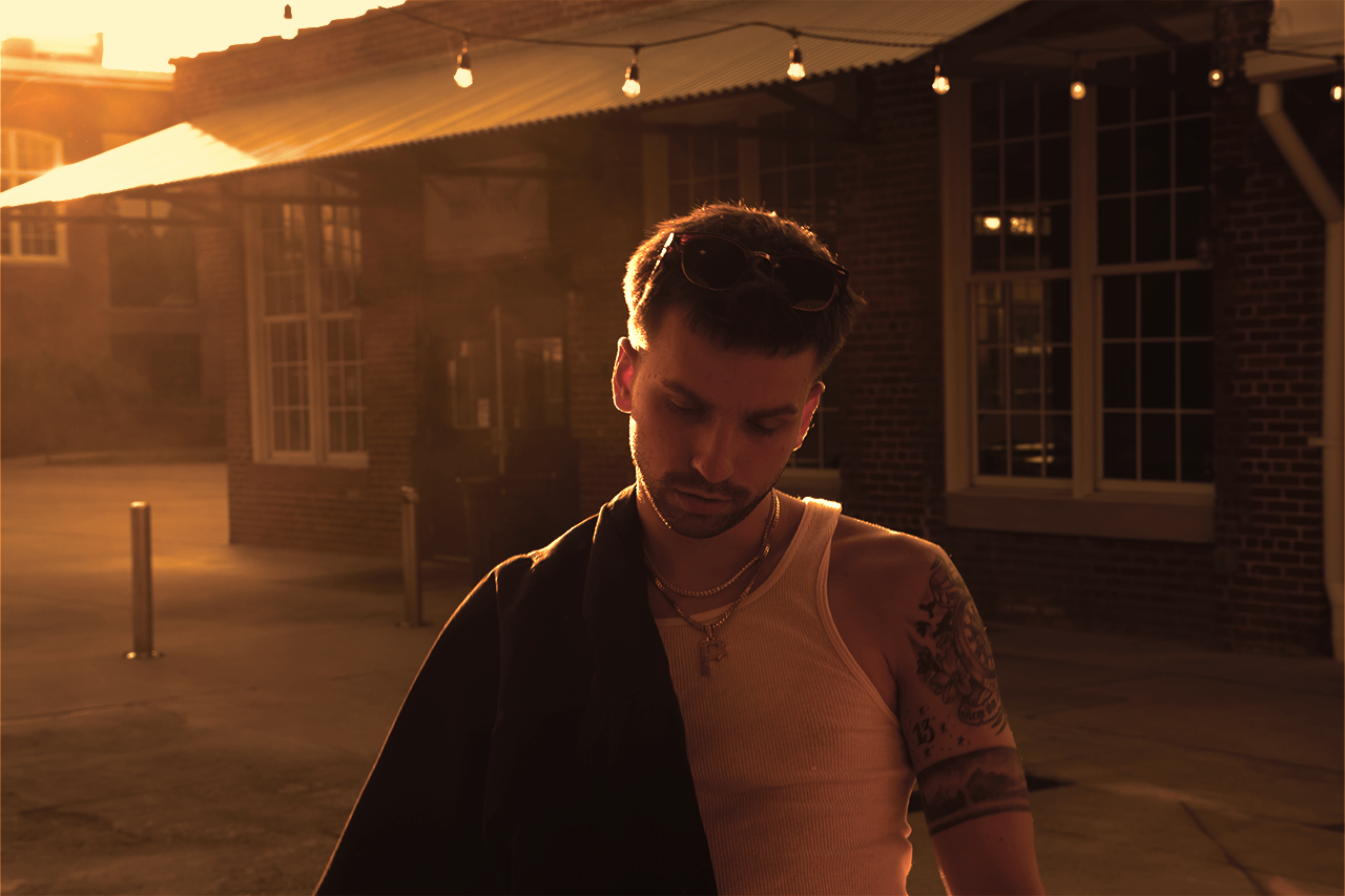 Young man staring deep in thought during the evening light with a jacket hanging over his shoulder