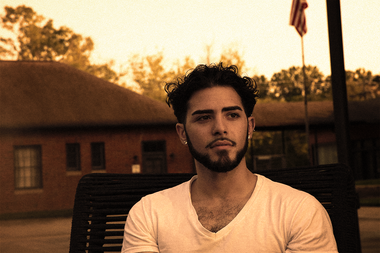 Young man in white t shirt sitting on a bench in front of a flagpole