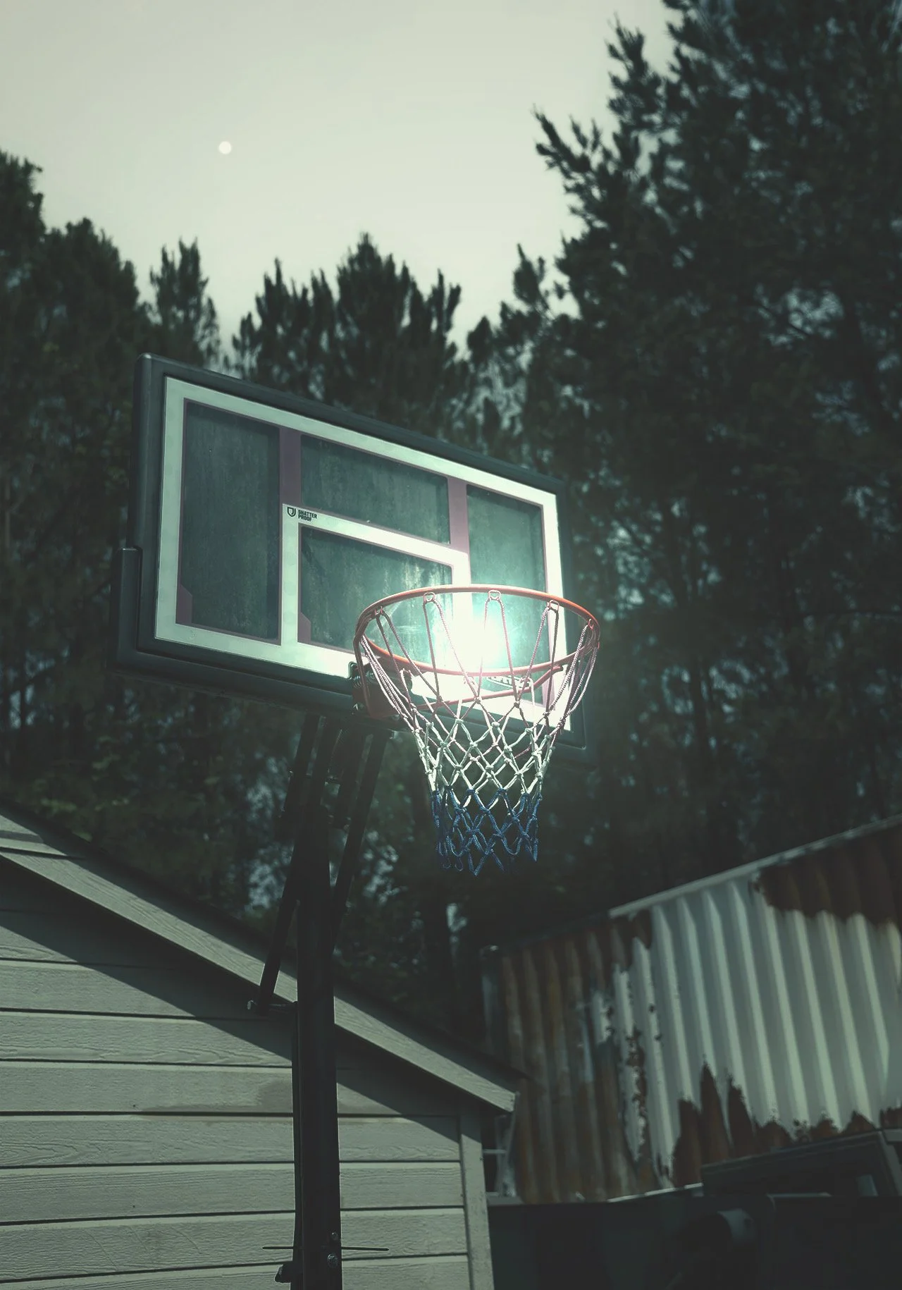A basketball net with a surreal glow in the midst of blue hour