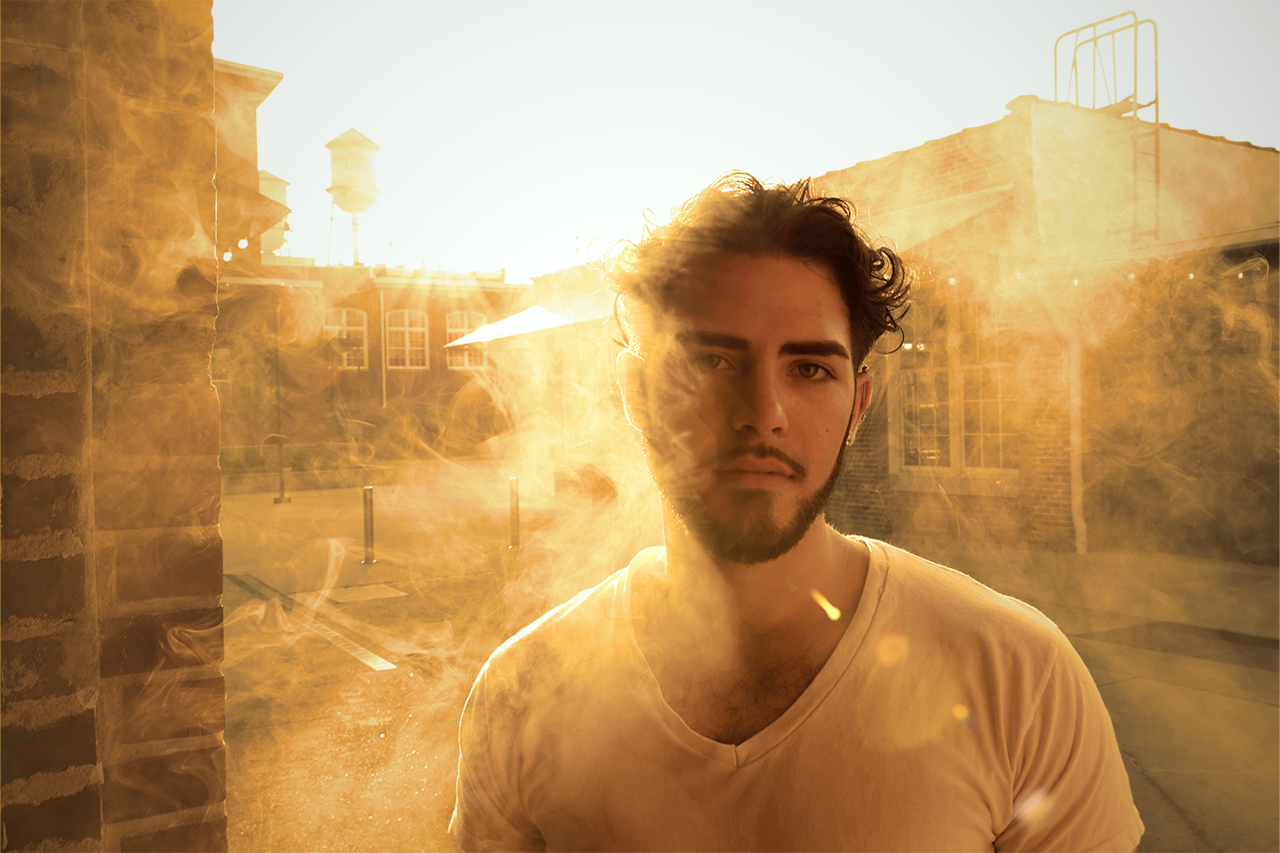 Young man standing in front of a hazy, golden hour background