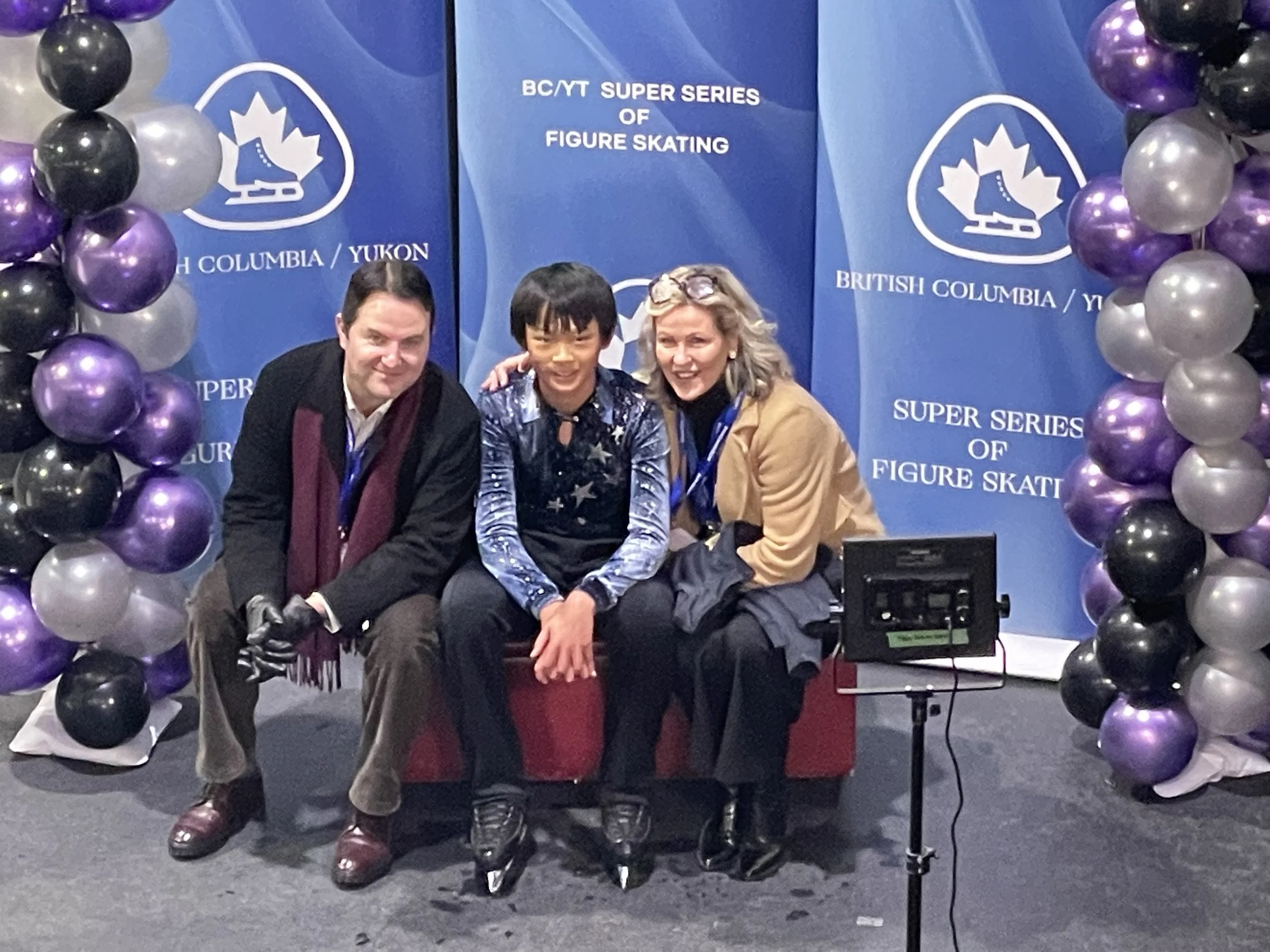 RCV skater Nathan Guo sits with coaches Deena Beacom and Matt Willis in the kiss and cry waiting for his scores