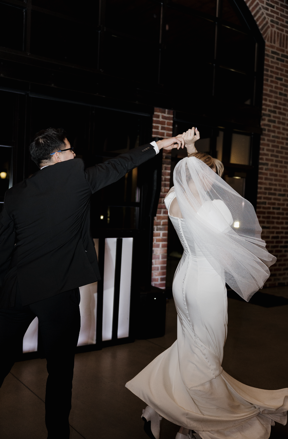 Bride and groom dancing together at a Utah wedding reception with a brick wall backdrop
