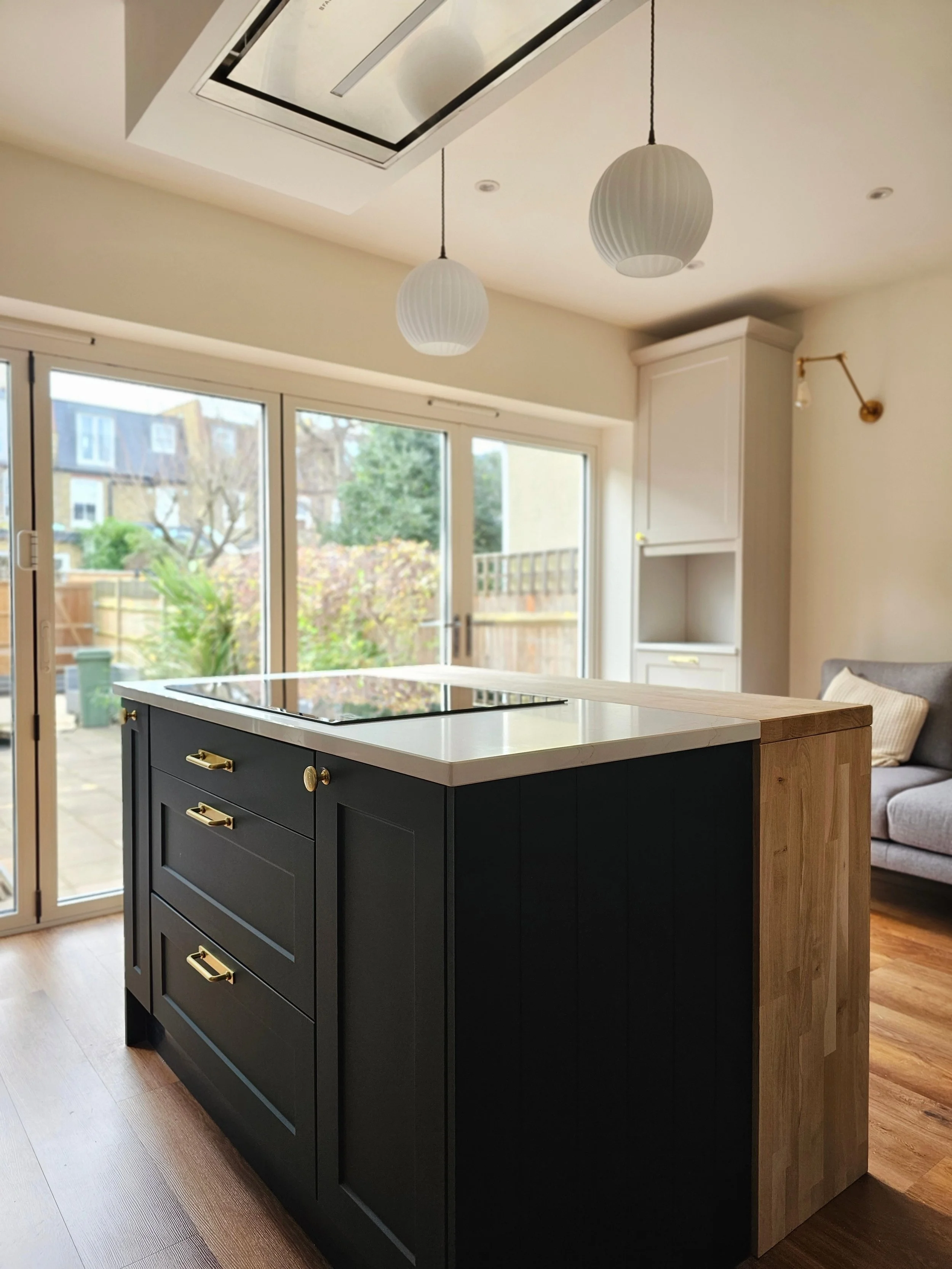 Deep green Shaker kitchen with warm oak, brass handles, fluted glass and a light-filled island.