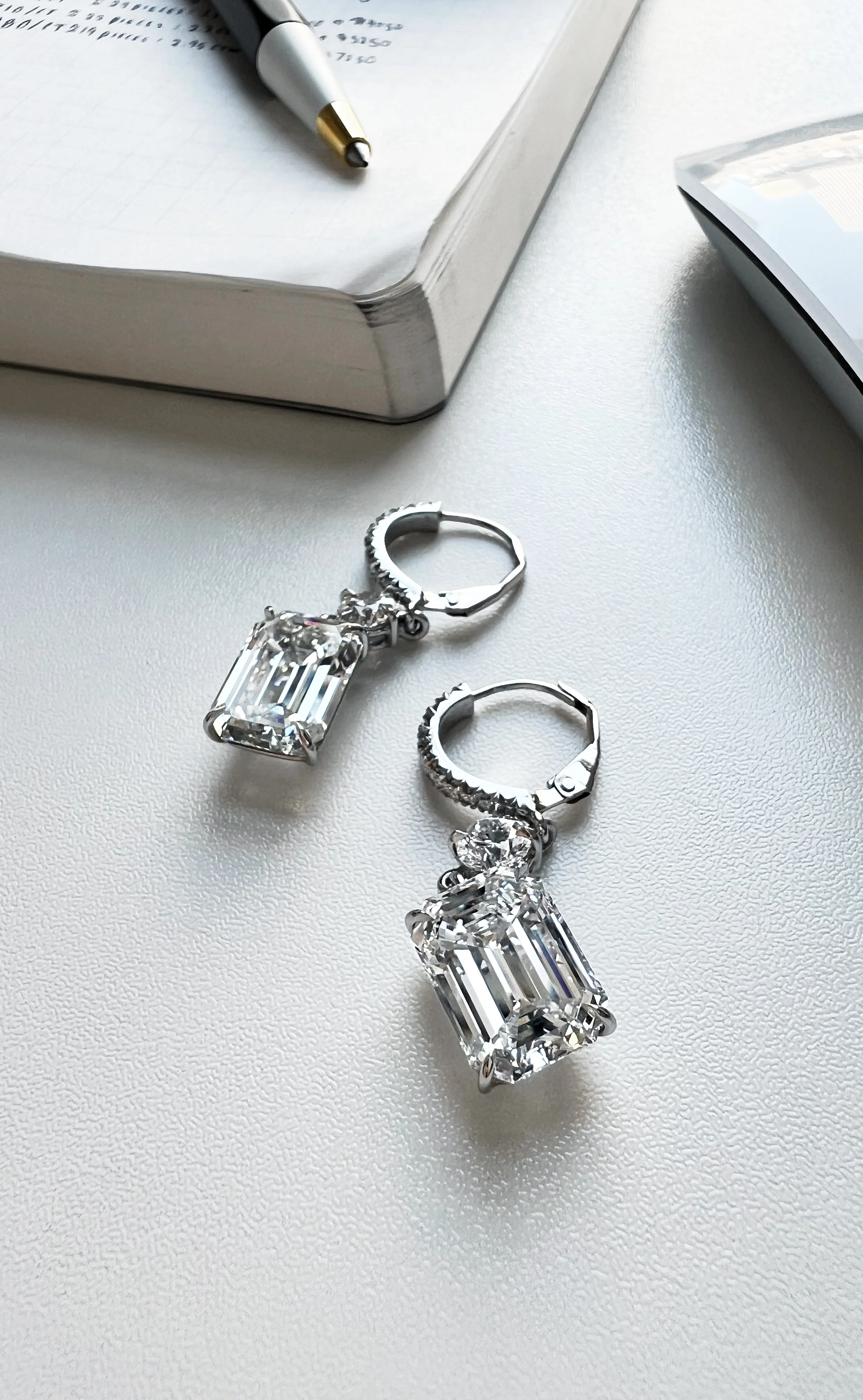 Matched pair of 7-carat natural emerald-cut diamond drop earrings (14 ctw) set in 18K white gold with 0.60 ct round brilliants. Rare scale and high-jewelry presence.