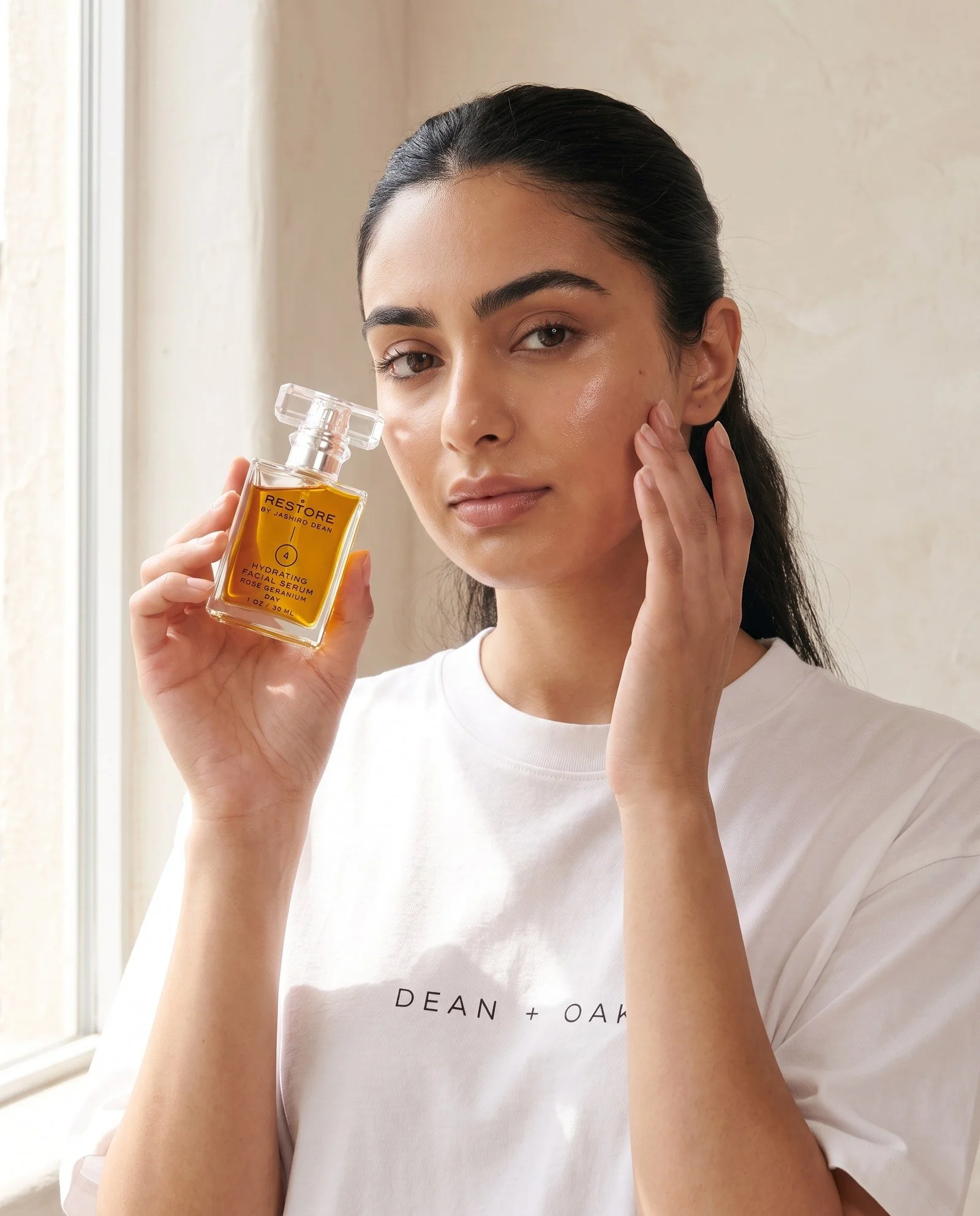 Dean + Oak RESTORE Hydrating Facial Serum, held by a model