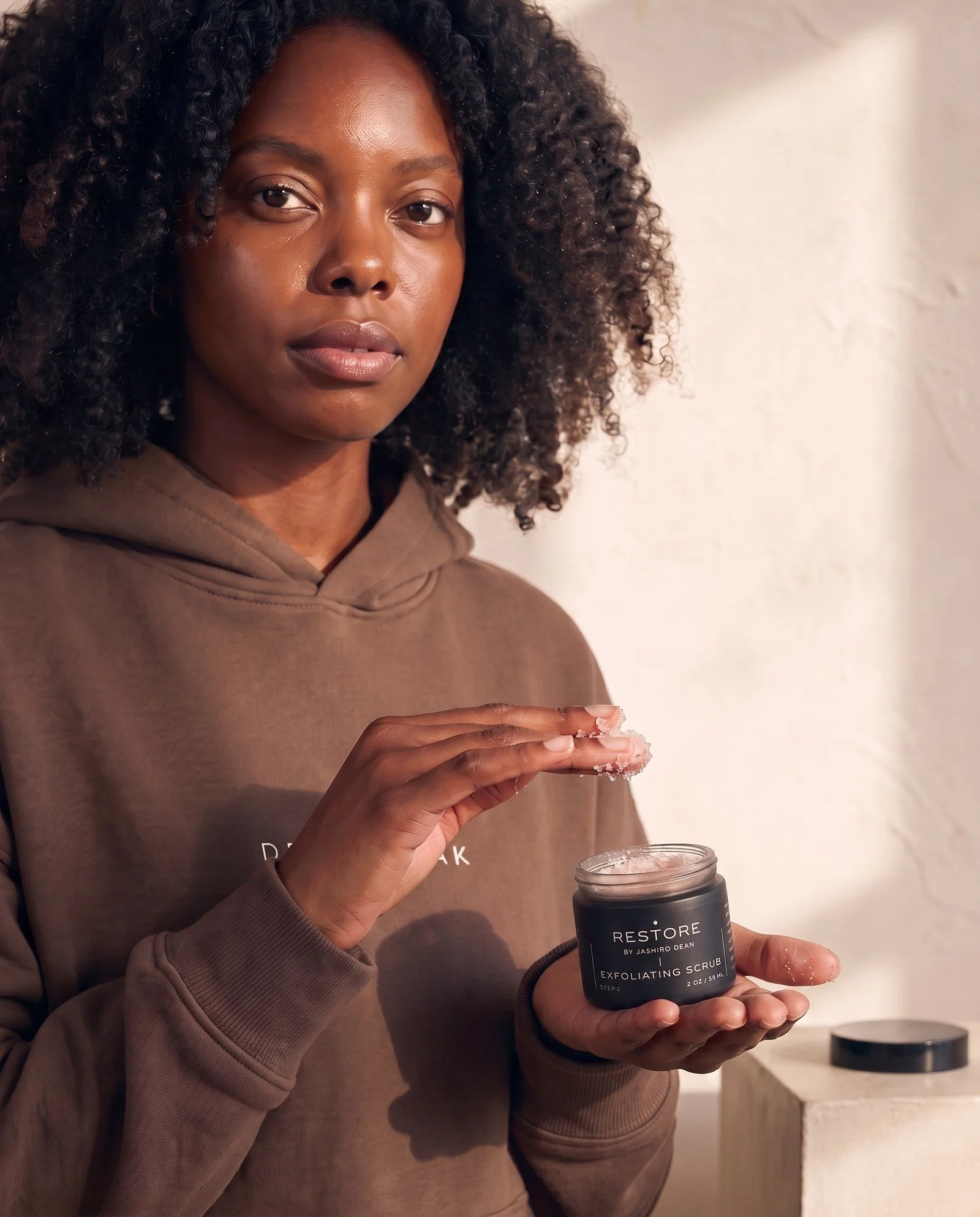 Dean + Oak RESTORE Exfoliating Scrub, held by a model
