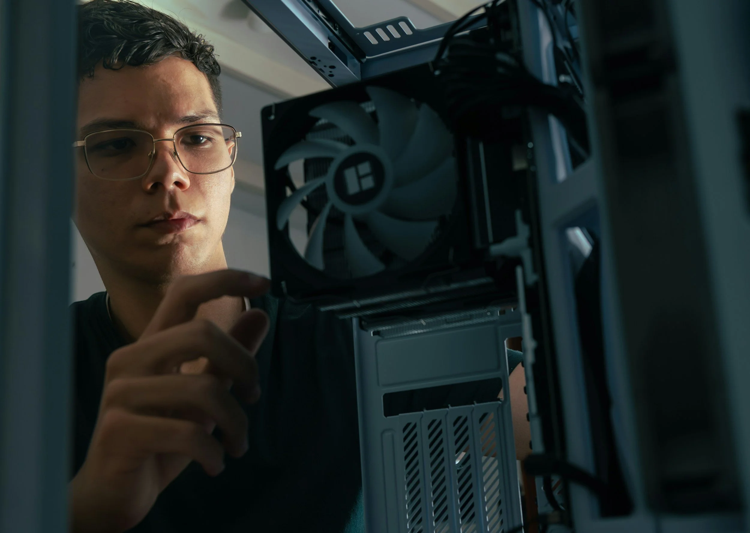 a computer repair person wearing glasses working inside a desktop computer with a case fan visible