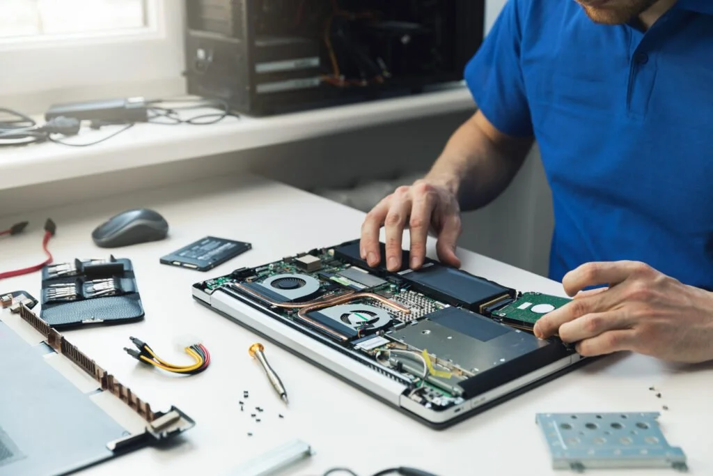 Person repairing a laptop on a desk, with electronic components and tools