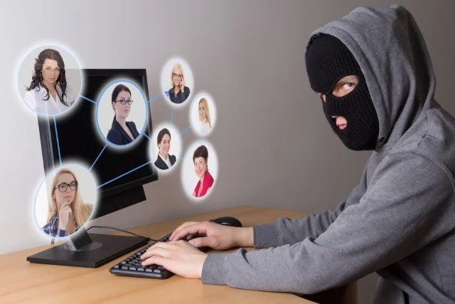 Person in a ski mask at a computer with floating images of women on the screen, concept of cybercrime or hacking.