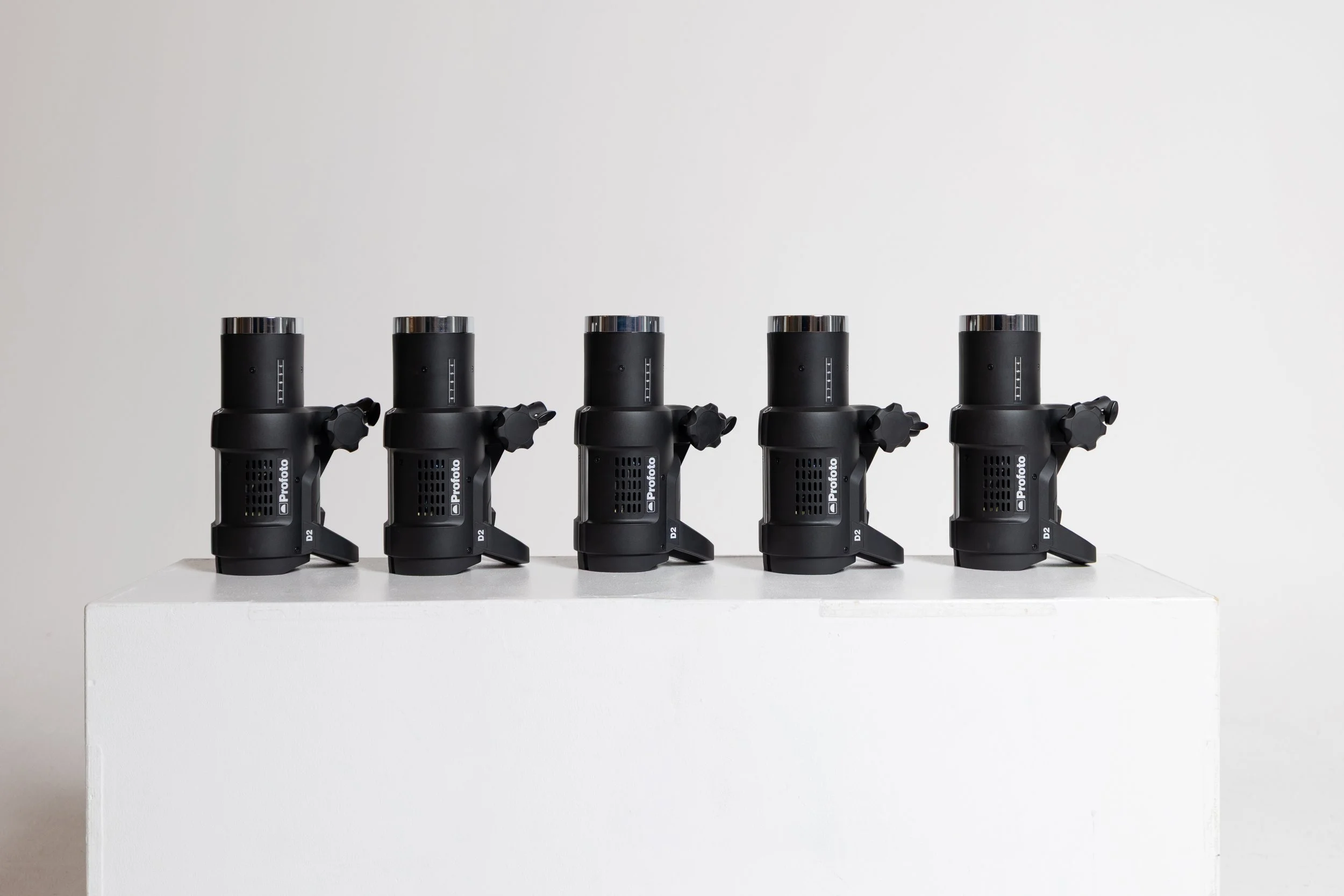 Three black professional camera stabilizers with handles and adjustment knobs are placed on a white platform against a plain gray background.