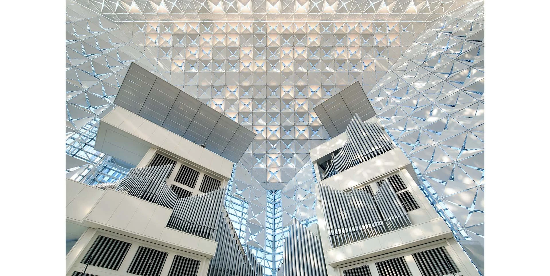 Interior view of a Cathedral with an intricate geometric ceiling pattern and large structures with metallic and white finishes.