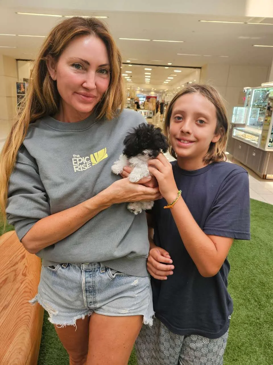 A woman and a boy holding a small black and white teacup poodle puppy in a shopping mall.