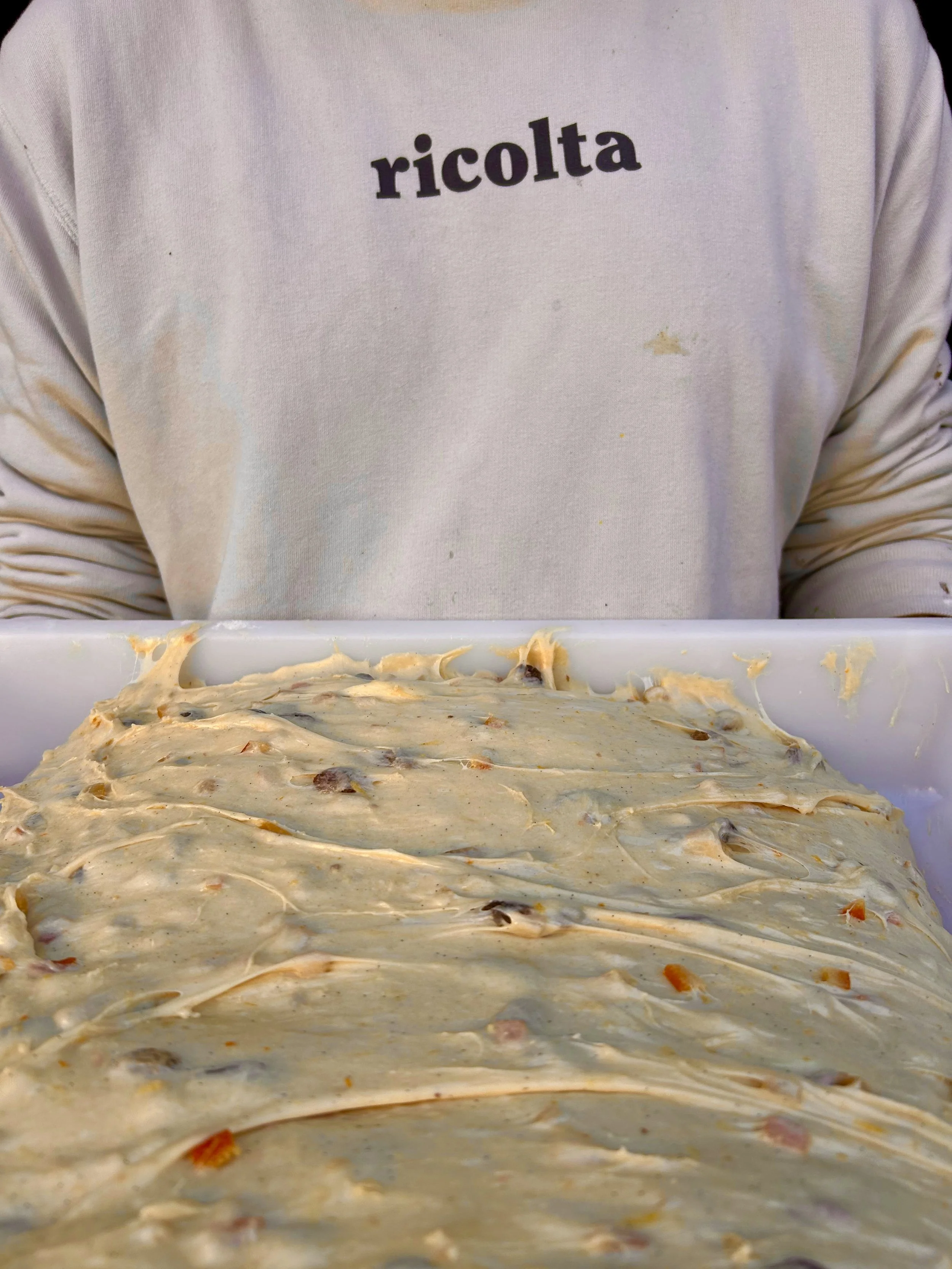 Un recipiente con masa de pizza lista para hornear, con ingredientes visibles dispersos en la superficie.