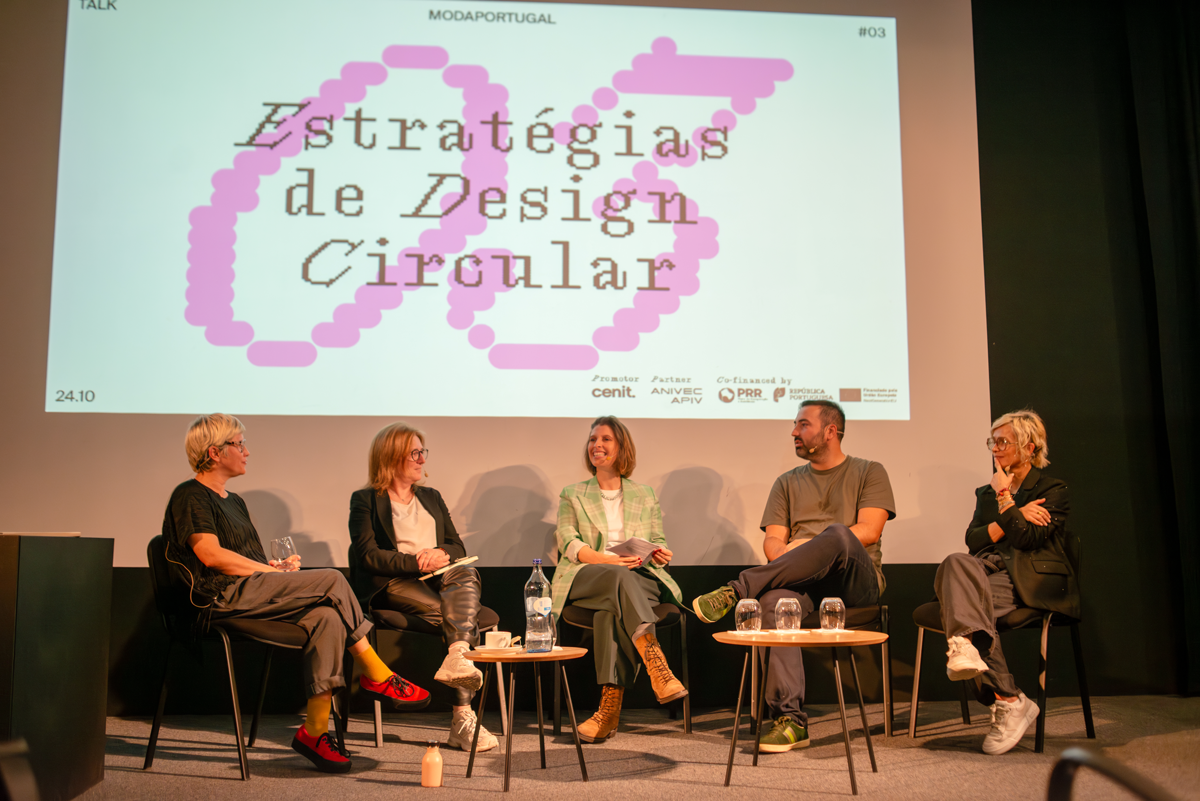 Painel com cinco pessoas sentadas em uma roda de discussão em frente a uma tela de projeção que exibe o texto 'Estratégias de Design Circular' em português, com ilustrações de círculos rosa ao redor.