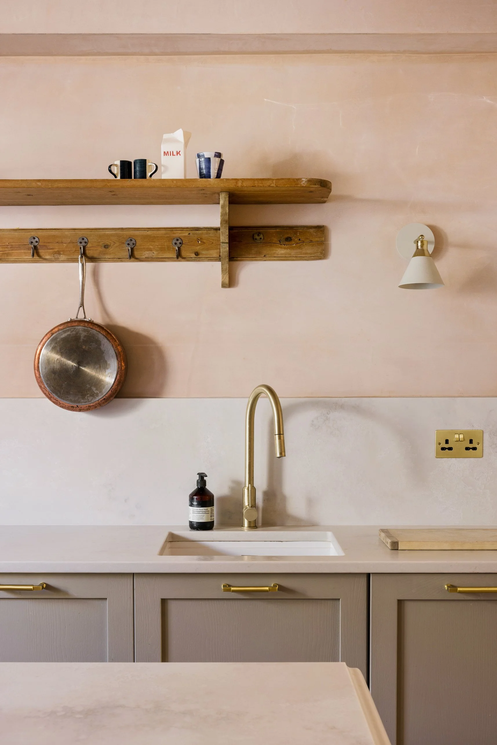 Kitchen detail with natural plaster walls, timber shelving, brass tap and painted cabinetry