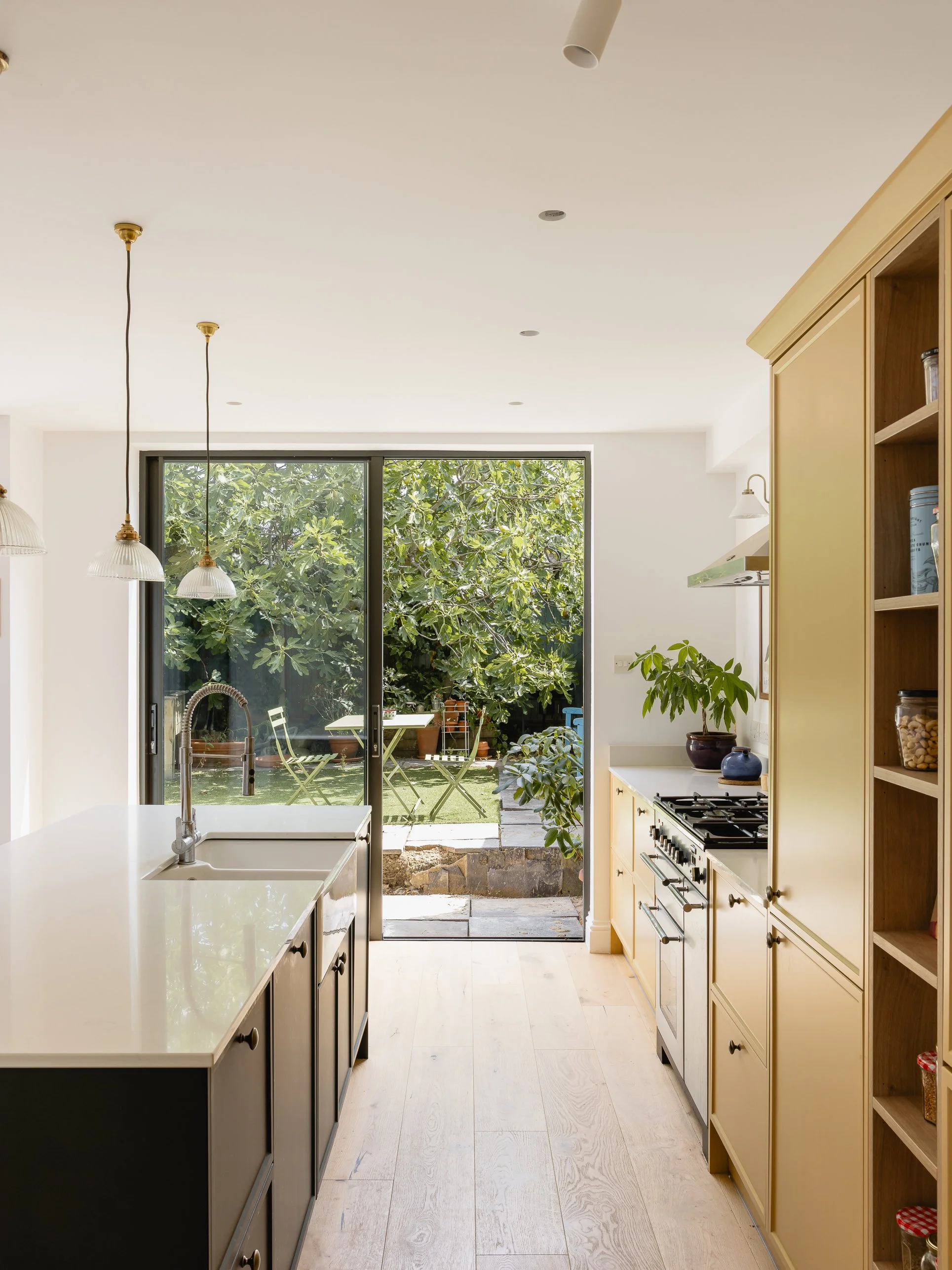 View through the renovated kitchen towards the garden, with large glazed doors, kitchen island and warm Shaker cabinetry.