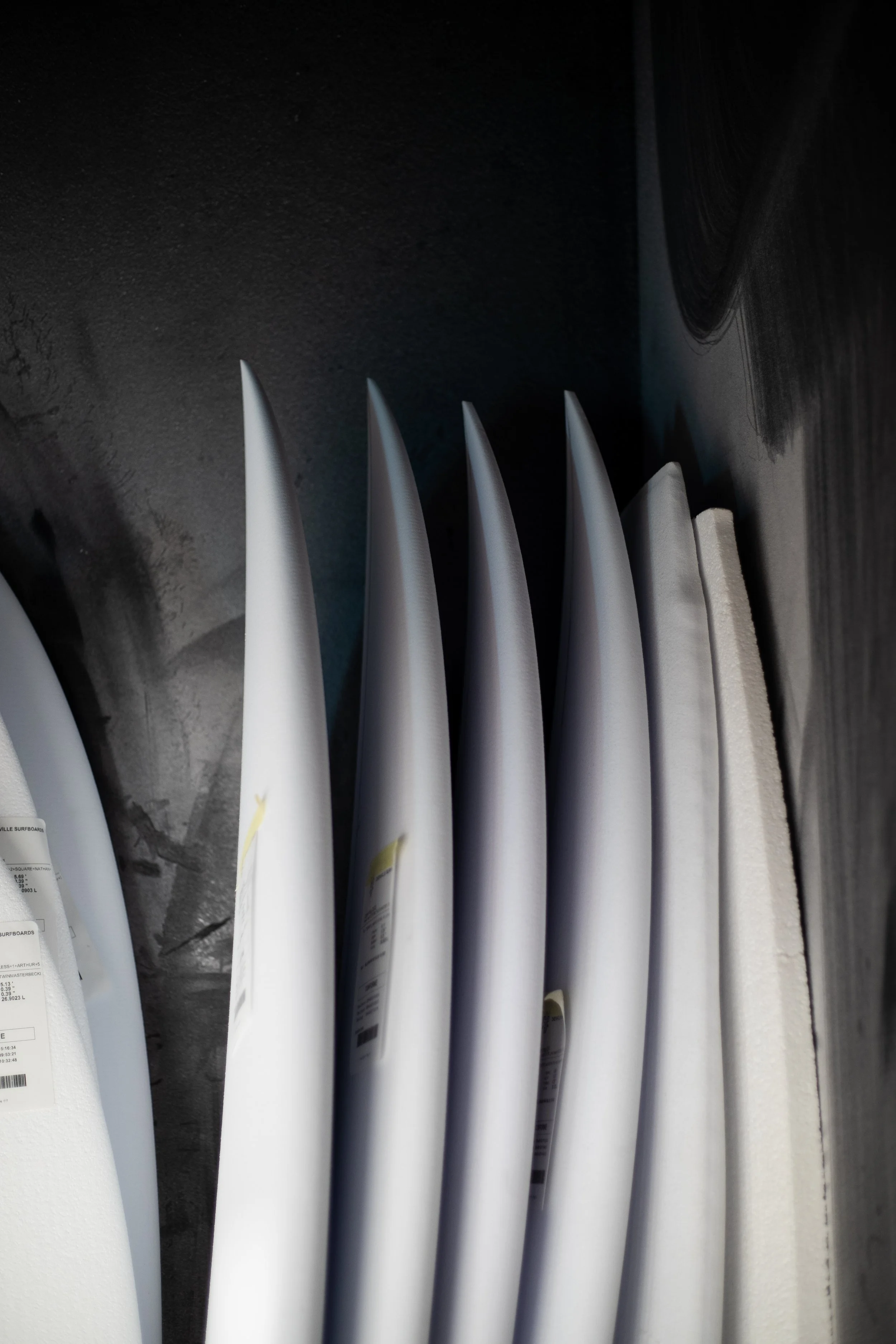 Dix planches de surf blanches rangées verticalement contre un mur en béton.