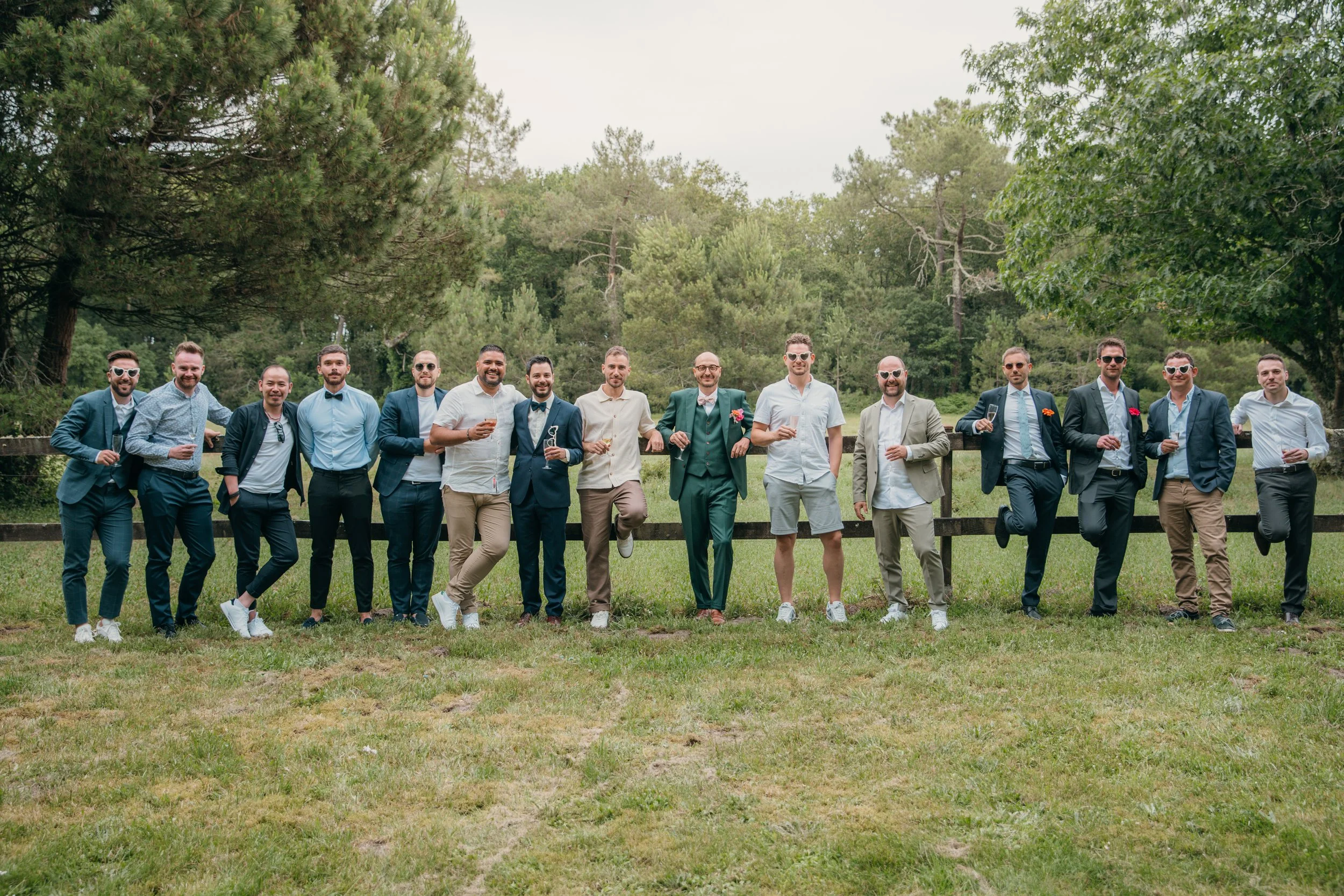 Groupe d'hommes en costume décontracté posant dans un parc lors d'un événement social ou d'un mariage.