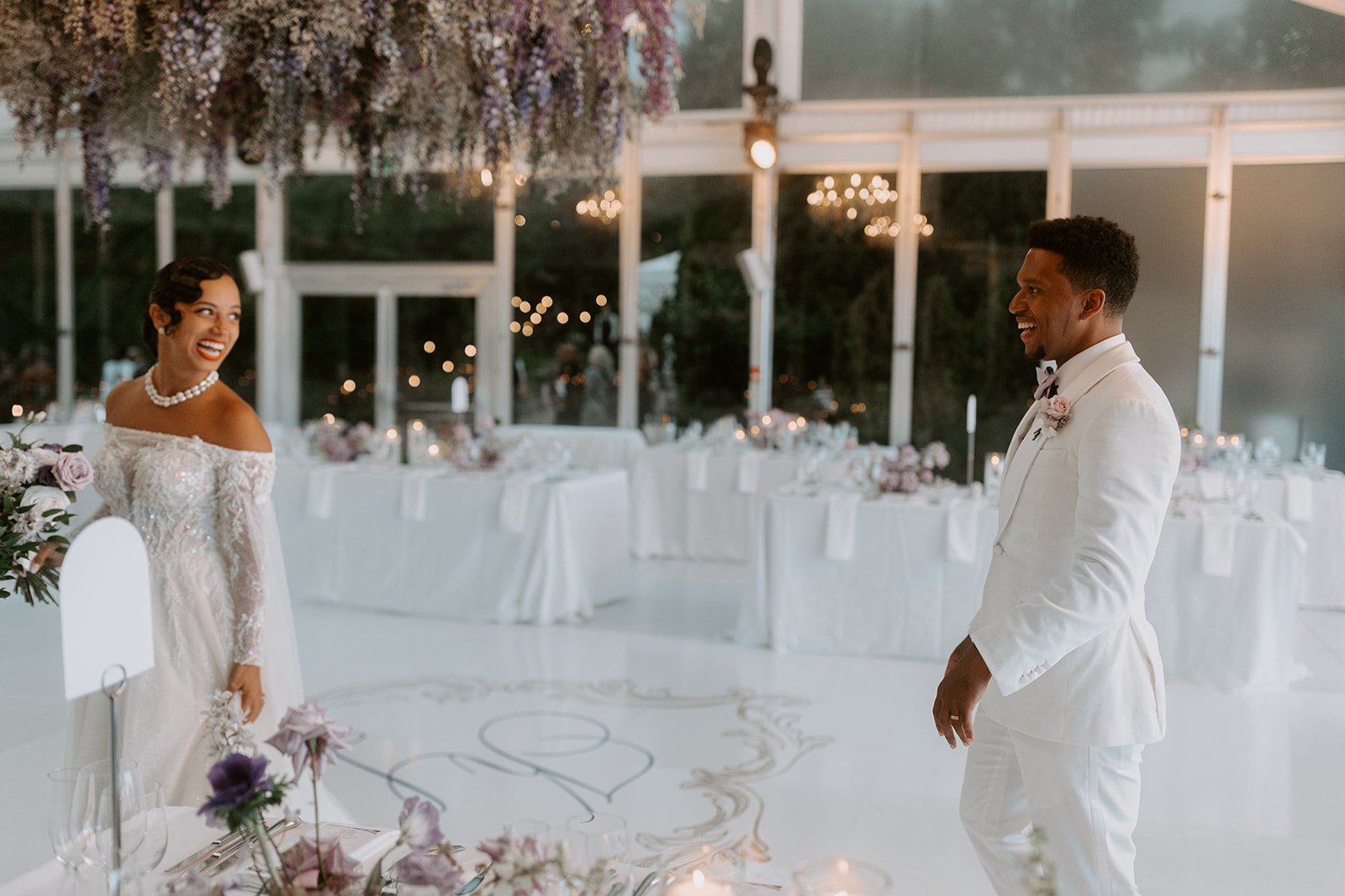 A bride and groom smiling at each other during their wedding reception in a beautifully decorated venue with floral arrangements, table settings, hanging flower installation Toronto Casa Loma
