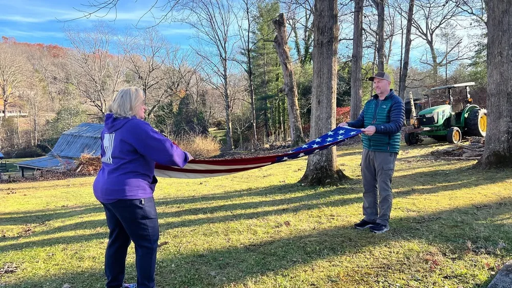 Veterans and volunteers holding an American flag together outdoors at the farm