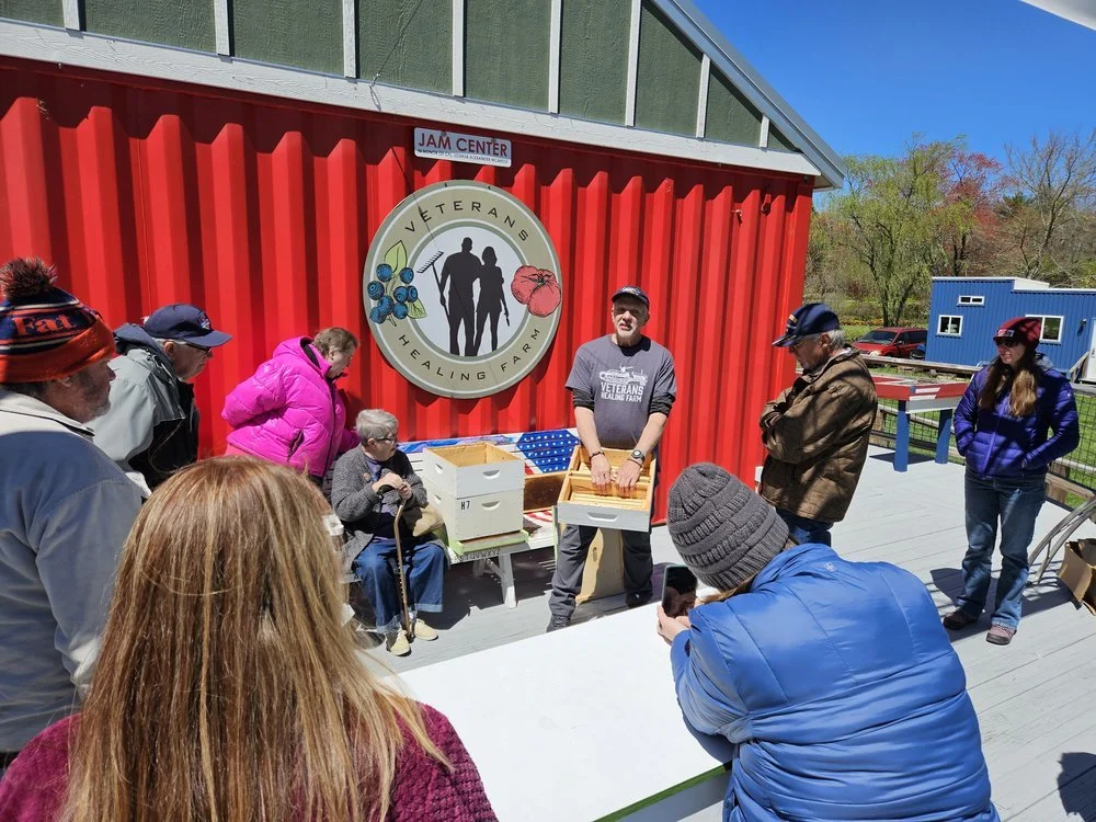 Veterans and guests gathered at an outdoor event in front of the farm's red barn