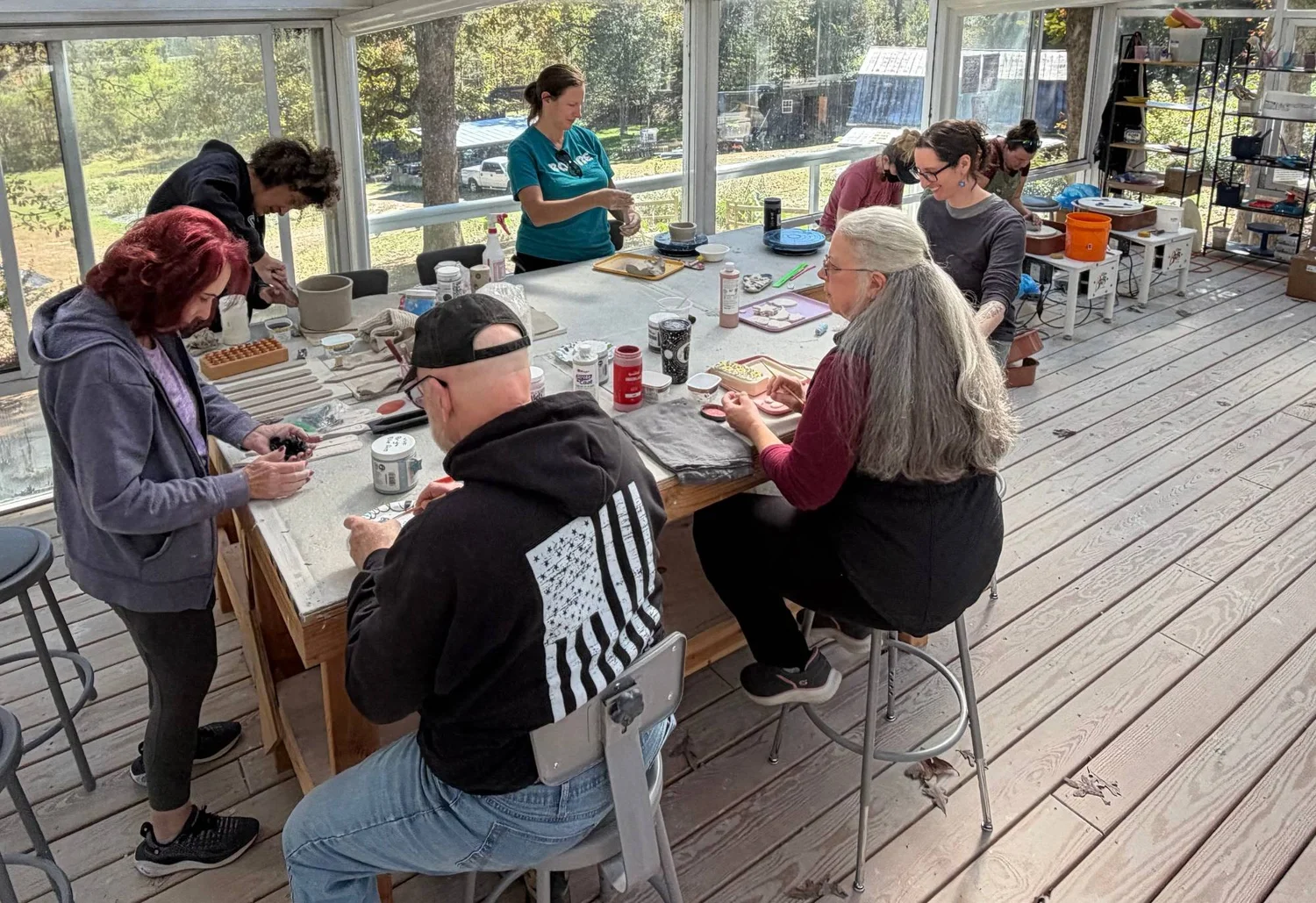 Veterans, family members, and volunteers working with clay around a big table in the farm's sunlit pottery studio