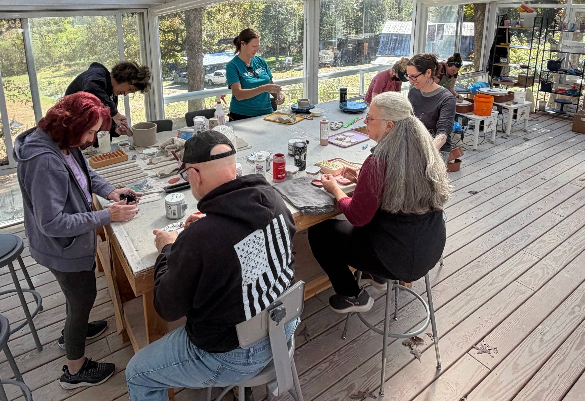 Veterans, family members, and volunteers working with clay around a big table in the farm's sunlit pottery studio