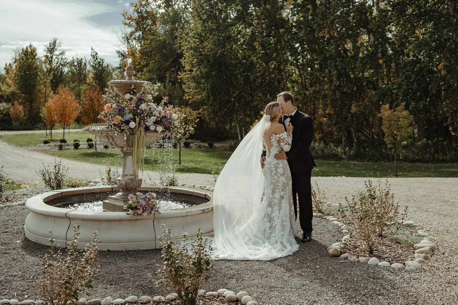 A bride and groom share a romantic kiss near the famous fountain in front of the Sparrow Lane Wedding Venue near Edmonton