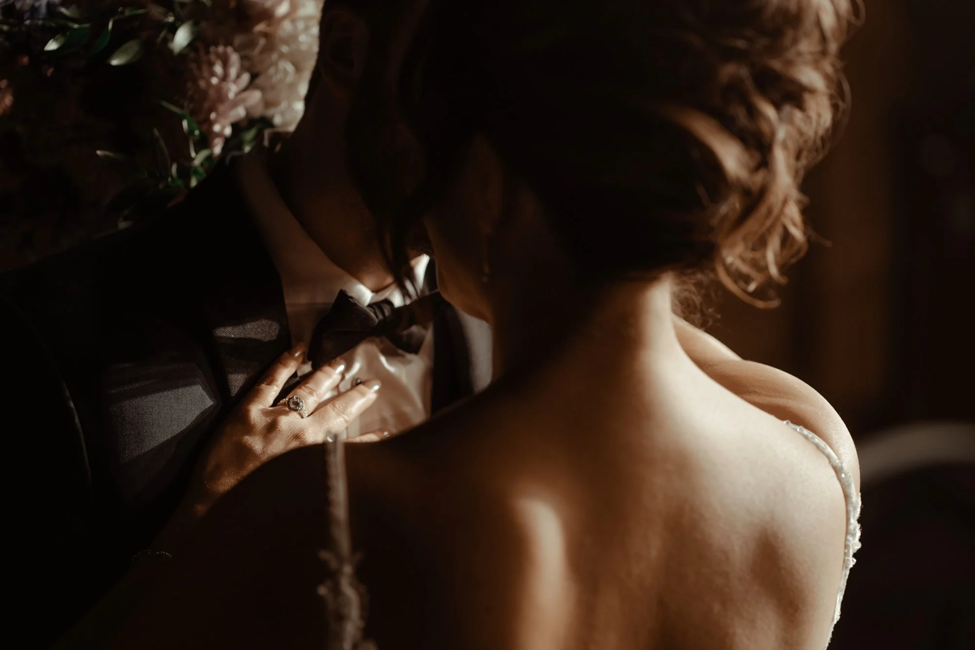 A bride holds her groom close while her diamond ring sparkles in the light as it lays on his chest.
