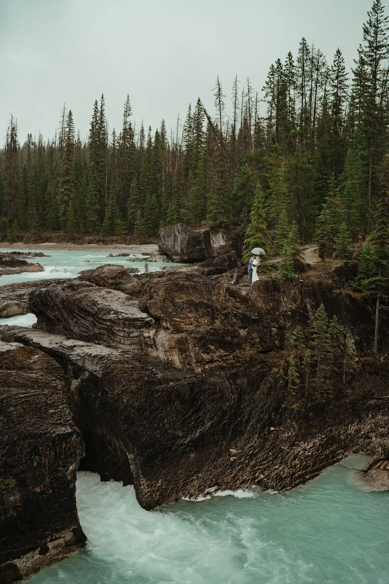 A bride and groom share a kiss while standing on the natural bridge that spans the kicking horse river below Emerald Lake Lodge.